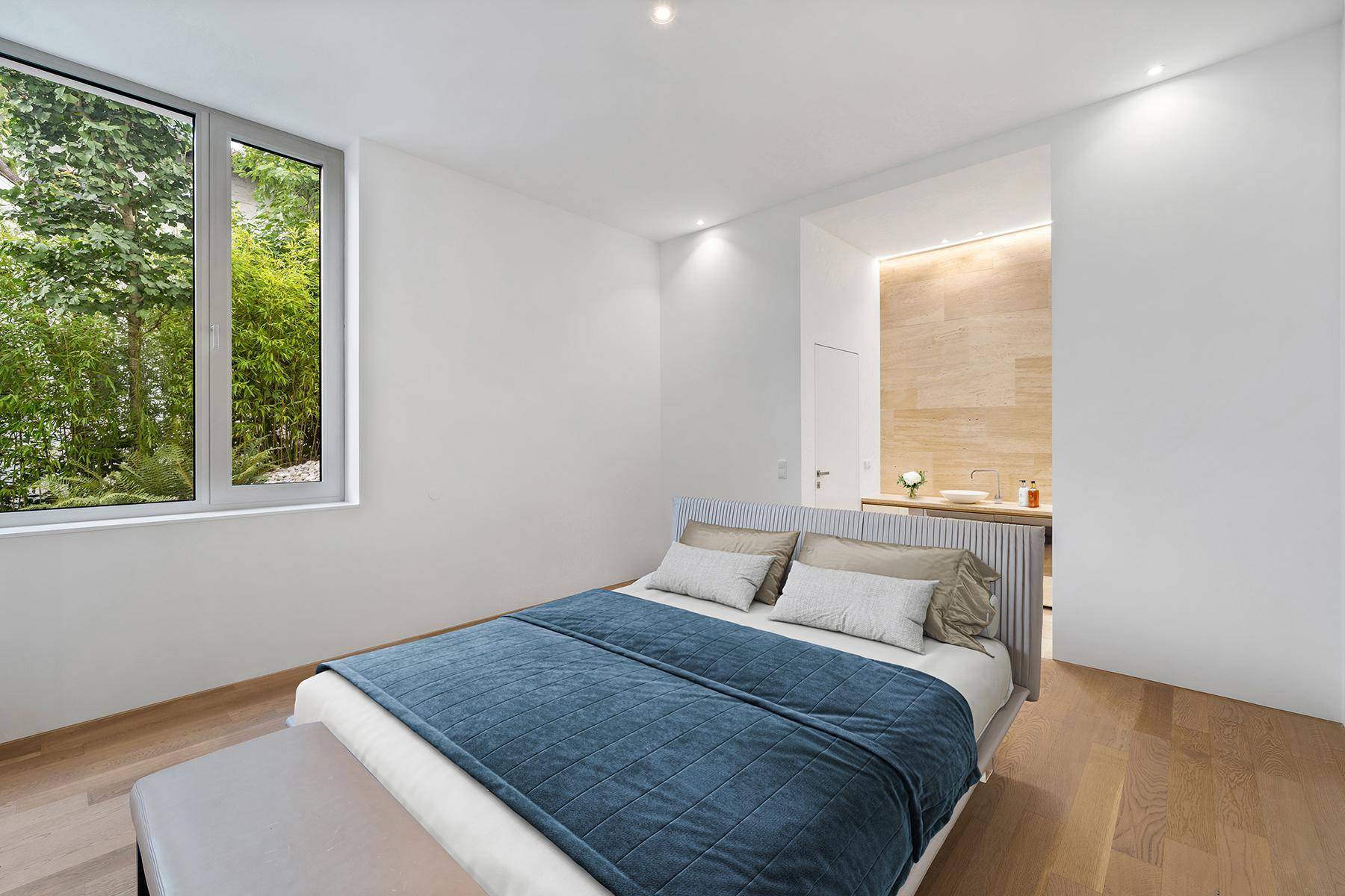 Schlafzimmer mit Holzboden und offenem Zugang zu einem modernen Badbereich mit Natursteinwand.