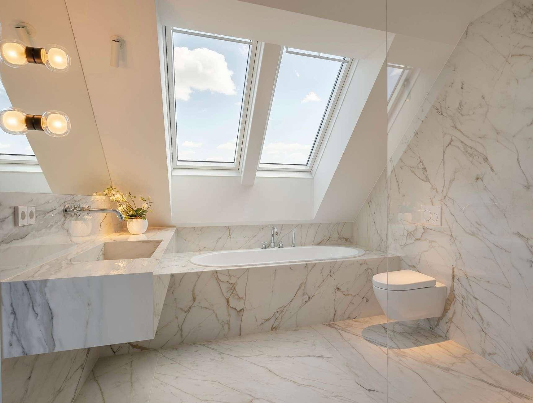 Luxuriöses Badezimmer mit Marmorfliesen, moderner Badewanne und zwei Dachfenstern für viel Tageslicht.
