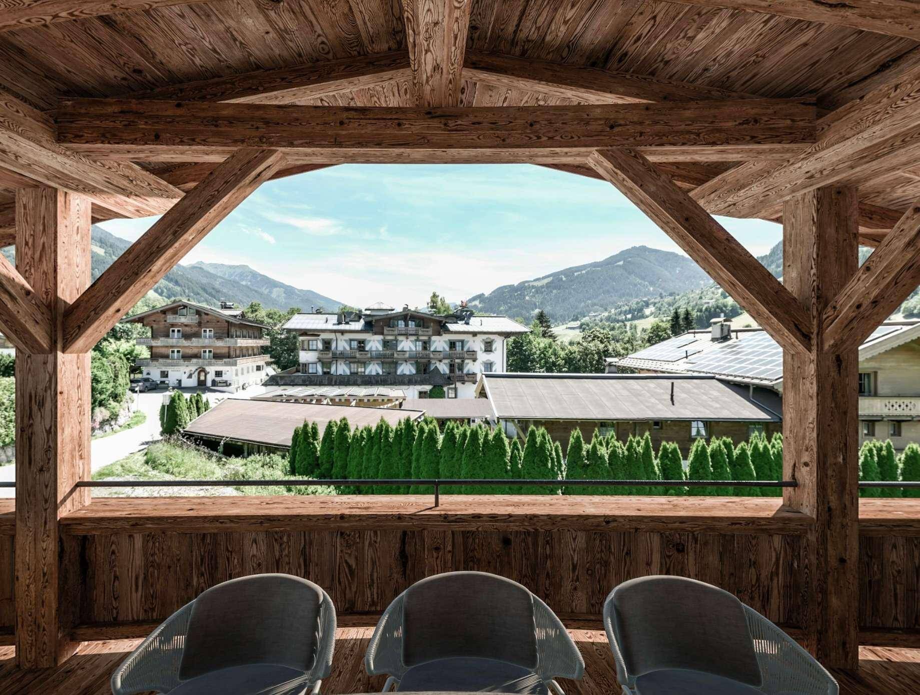 Blick vom Holzbalkon auf die umliegende Berglandschaft und das Dorf mit weiteren Gebäuden.