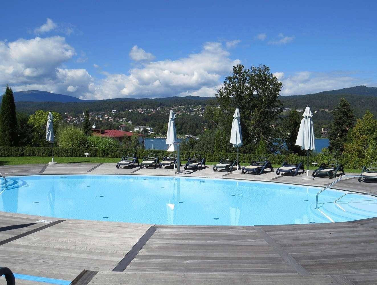 Großer Außenpool mit Liegestühlen, umgeben von Natur und mit Blick auf den See und die Berge.