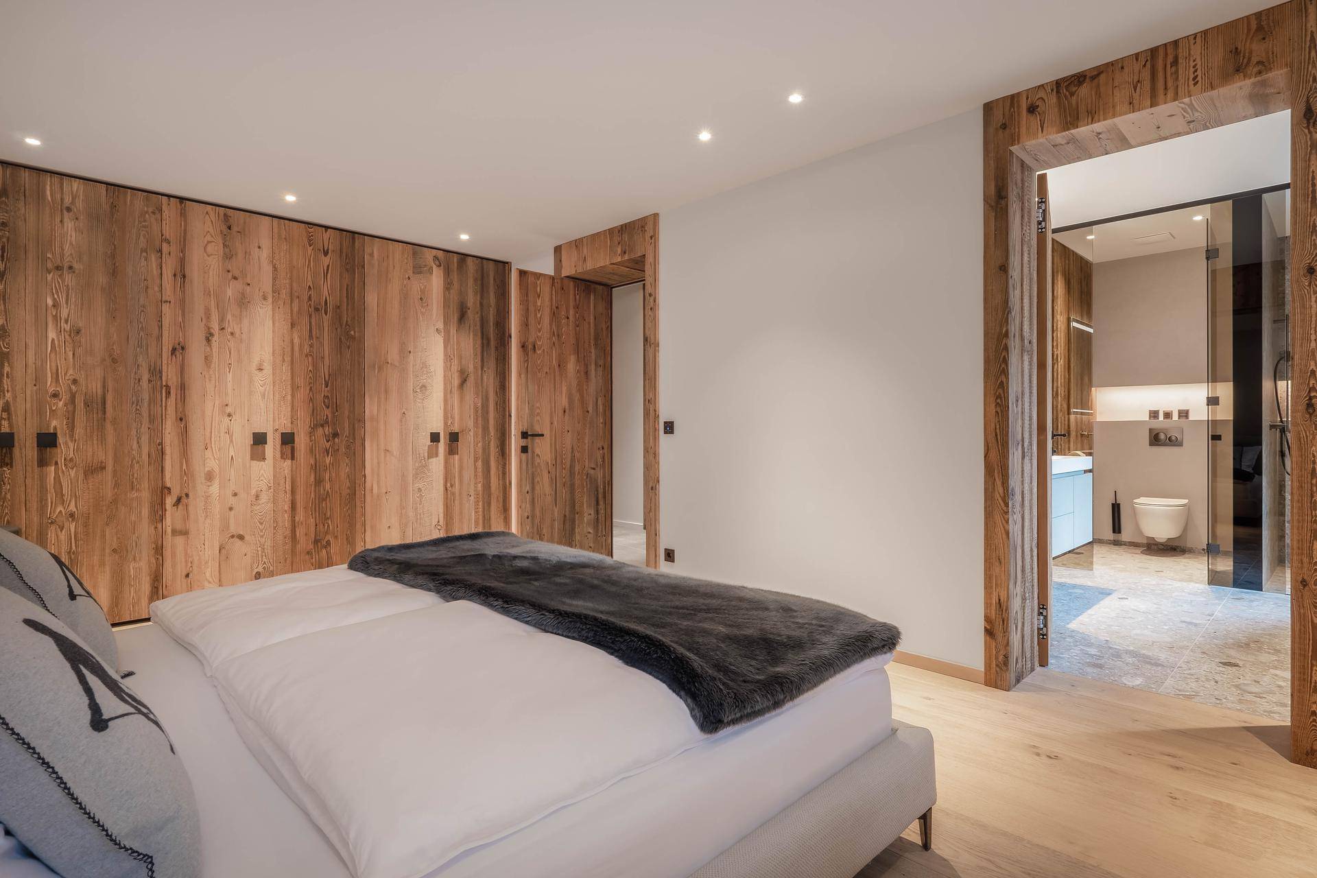 Schlafzimmer mit Holzwänden, Einbauschränken und direktem Zugang zu einem modernen Badezimmer.
