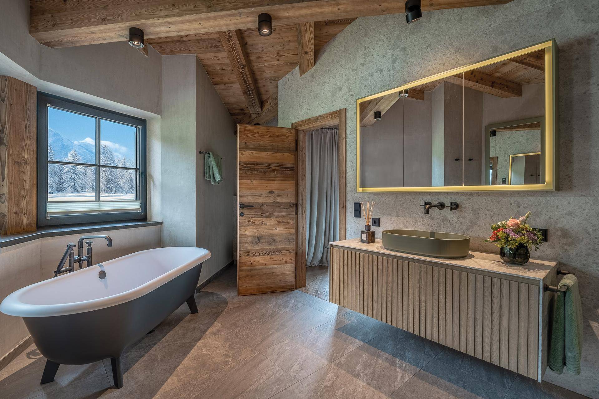 Modernes Badezimmer mit freistehender Badewanne, Holzbalkendecke und Fenster mit Bergblick.