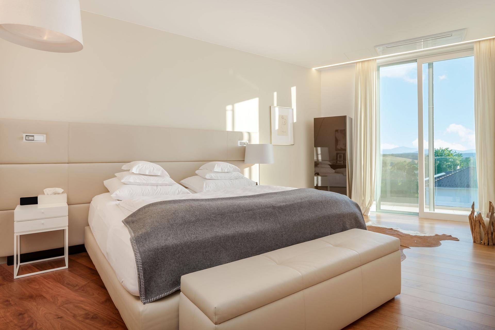 Helles Schlafzimmer mit großem Bett, Holzboden und raumhohen Fenstern, die einen weiten Blick in die Landschaft bieten.