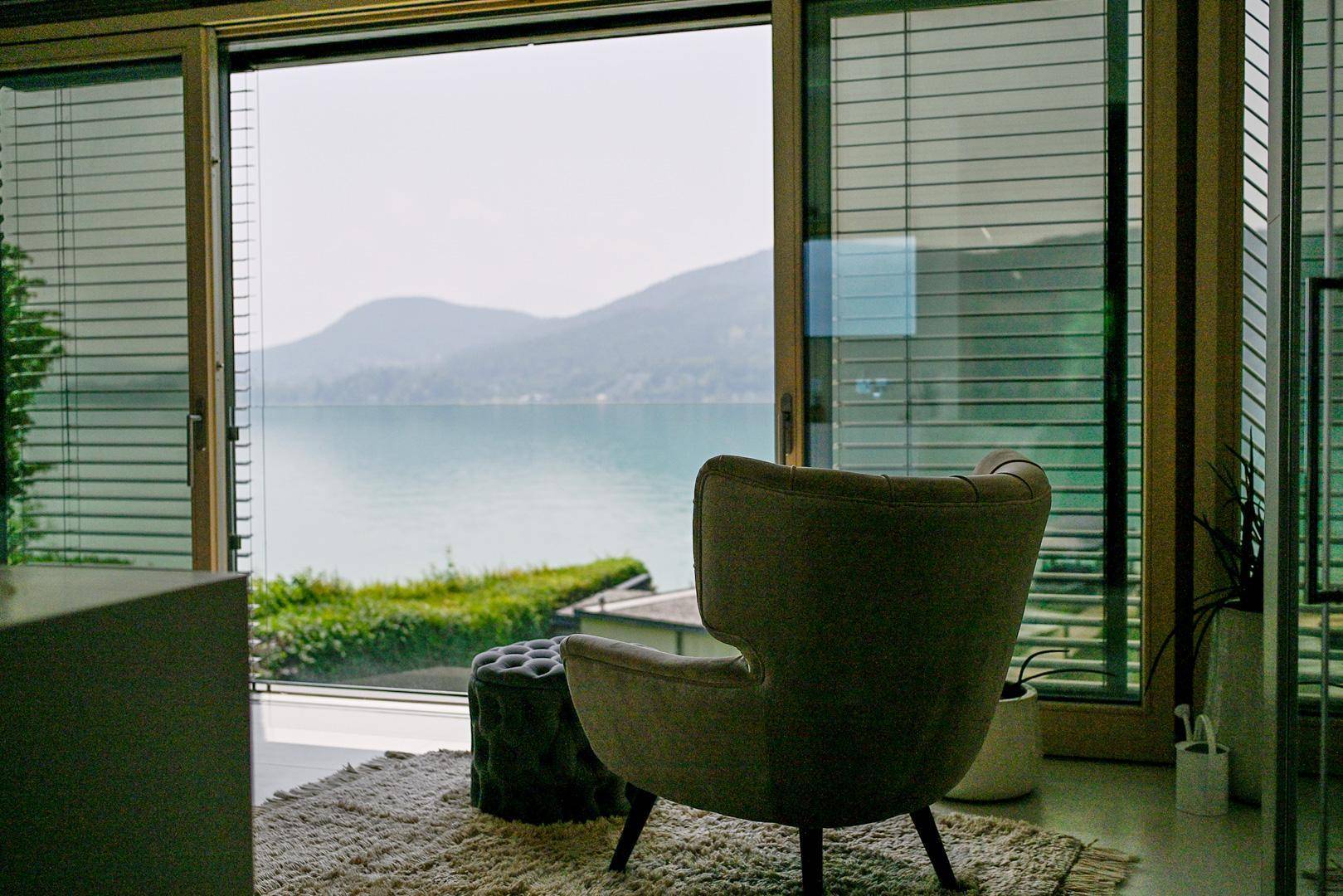 Gemütlicher Sessel am Fenster mit weitem Blick auf den See und die umliegenden Berge.
