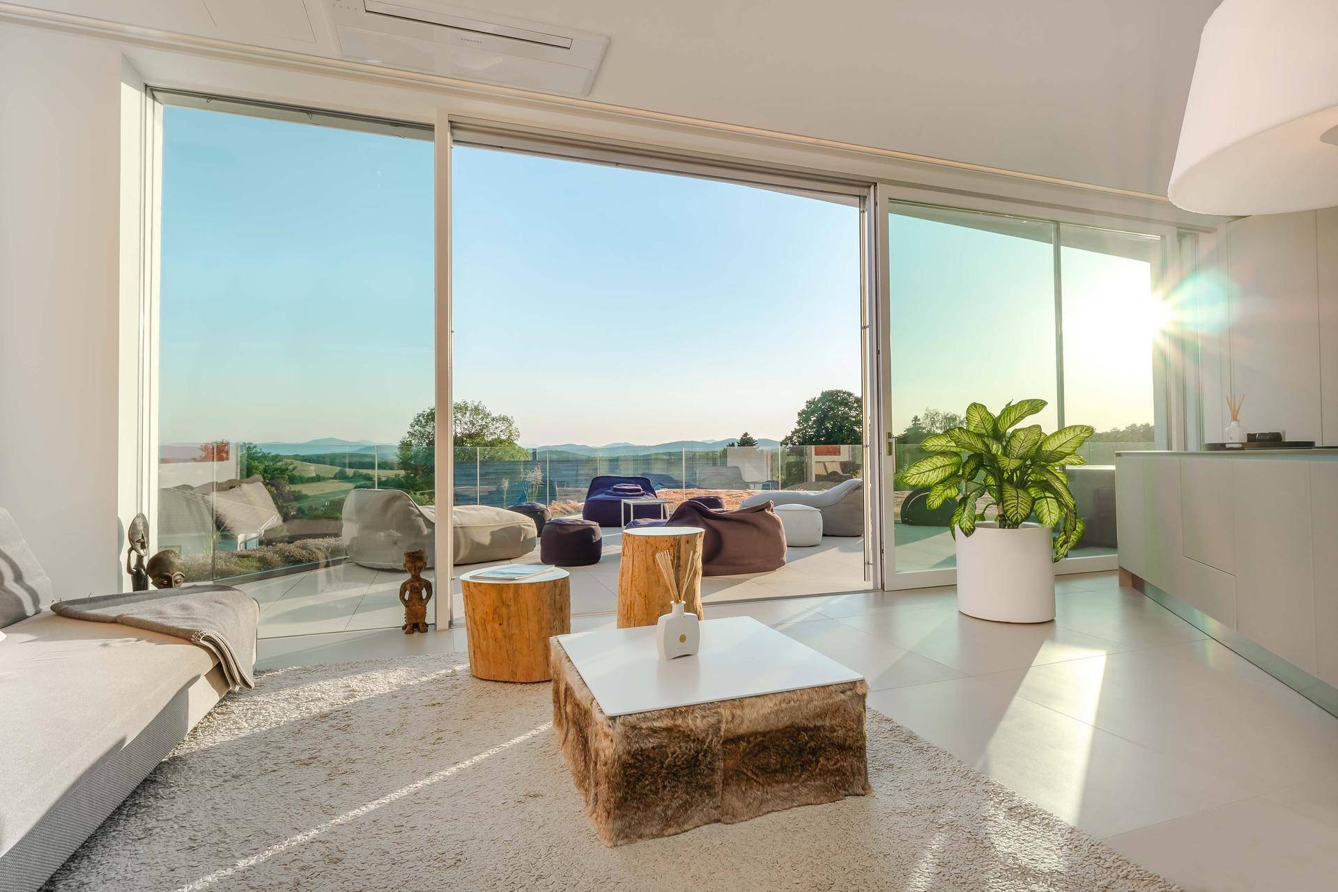Gemütlicher Wohnbereich mit Sofa und kreativen Tischen, offen zur Terrasse mit Sitzsäcken und weitem Ausblick.