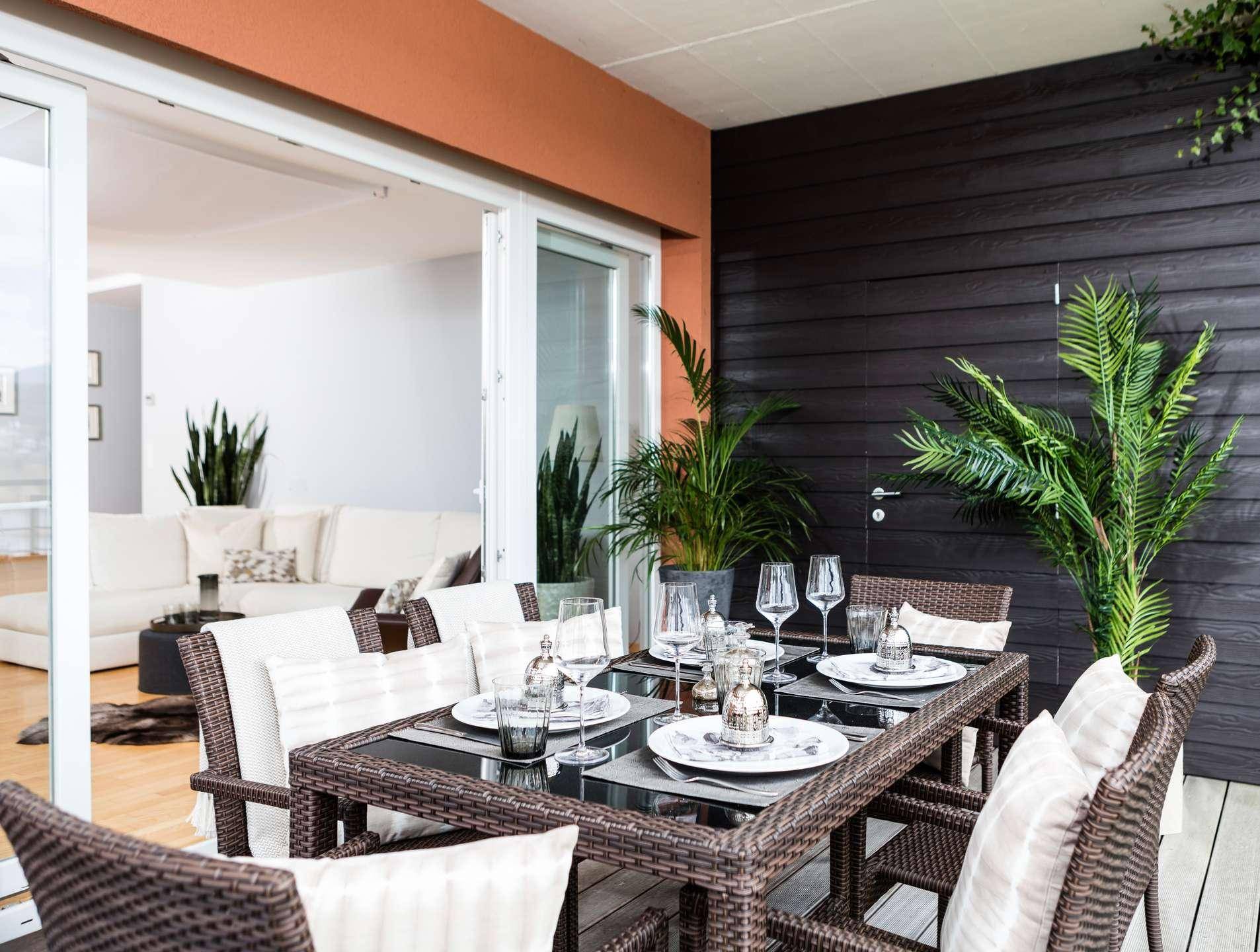 Möblierter Balkon mit Esstisch und Blick in den hellen Wohnbereich, ideal für Mahlzeiten im Freien.