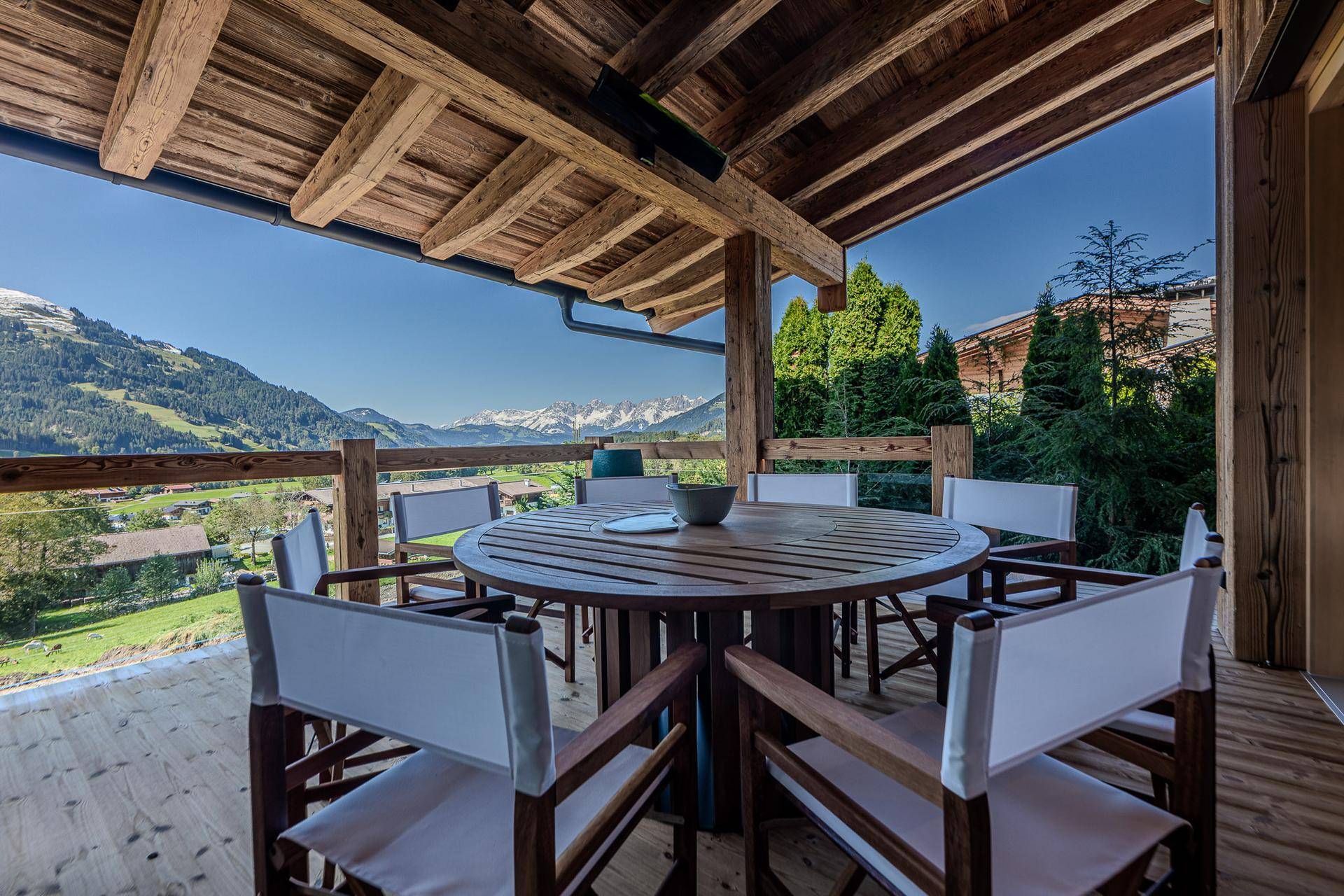 Überdachte Terrasse mit Holztisch, Stühlen und weitem Blick auf die umliegende Berglandschaft.