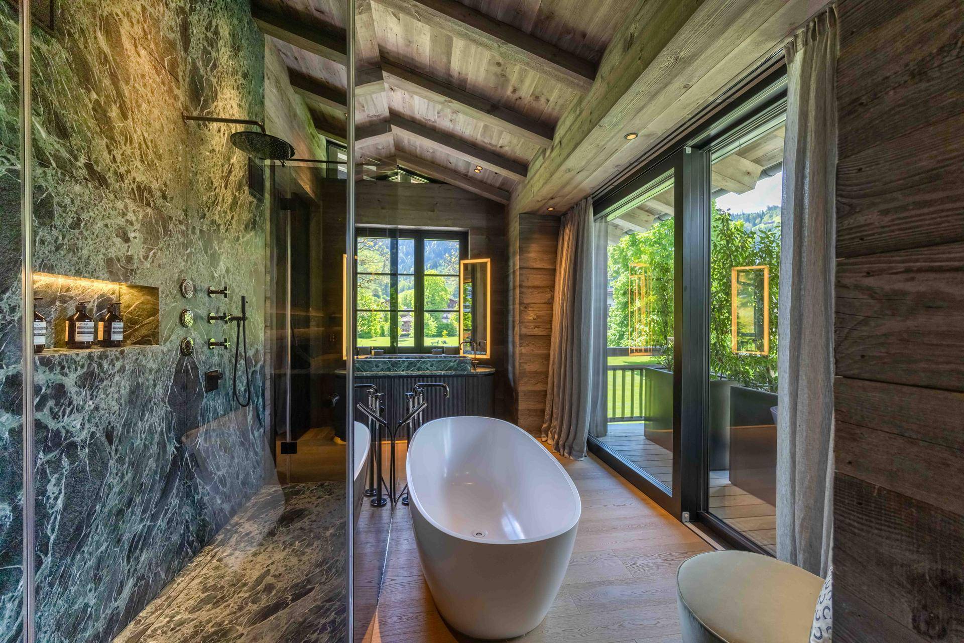 Luxuriöses Badezimmer mit freistehender Badewanne, Marmorwänden und Bergblick.