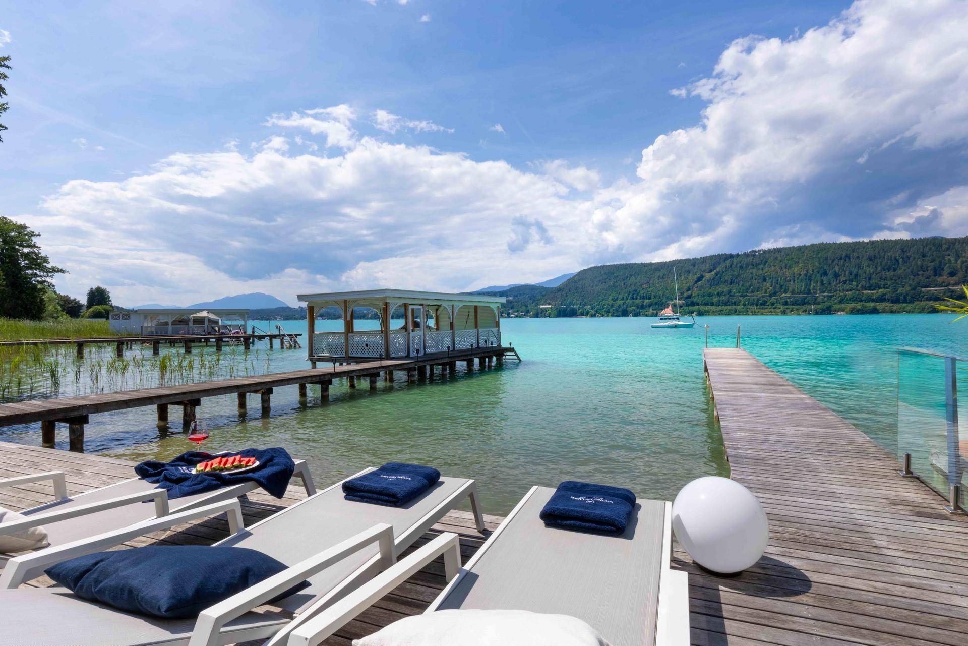 Sonnige Holzterrasse mit Liegestühlen direkt am See, bietet einen weiten Blick auf das Wasser und die Berge.