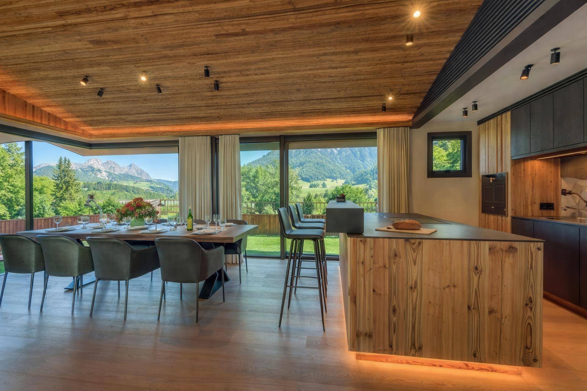Moderner offener Wohnbereich mit Holzboden, großer Küche und Esstisch mit Bergblick.