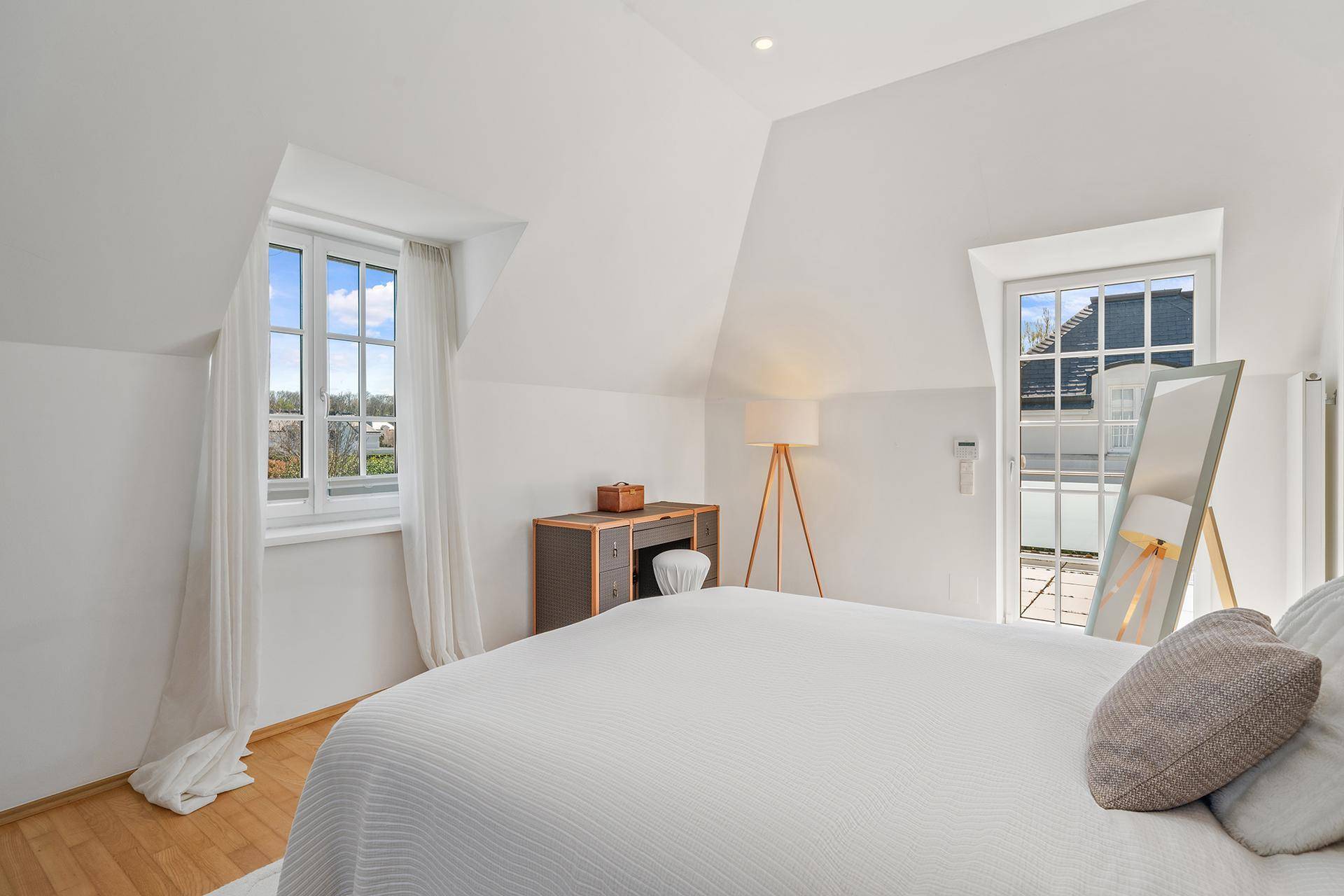 Gemütliches Schlafzimmer im Dachgeschoss mit Holzboden und viel natürlichem Licht durch die Fenster.