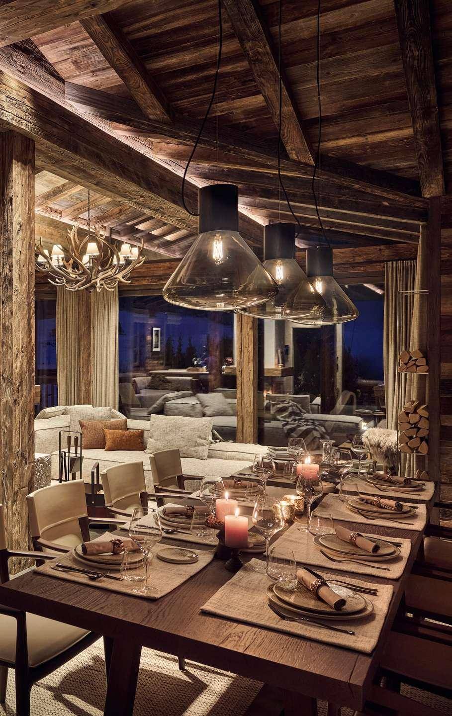 Gemütlicher Essbereich im alpinen Stil mit Holzbalken, gedecktem Tisch und Blick ins Wohnzimmer.