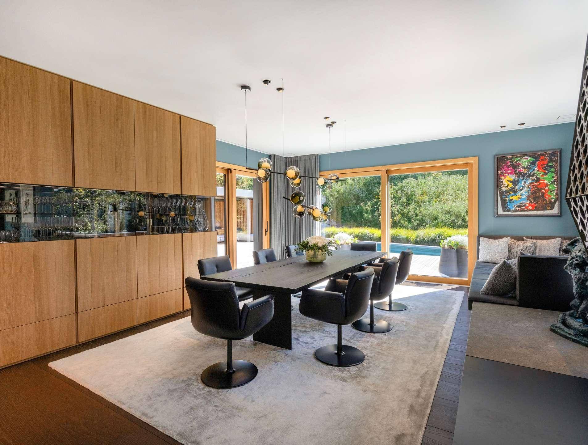 Moderner Essbereich mit Holzwand, großem Esstisch und Blick auf den Außenbereich mit Pool.