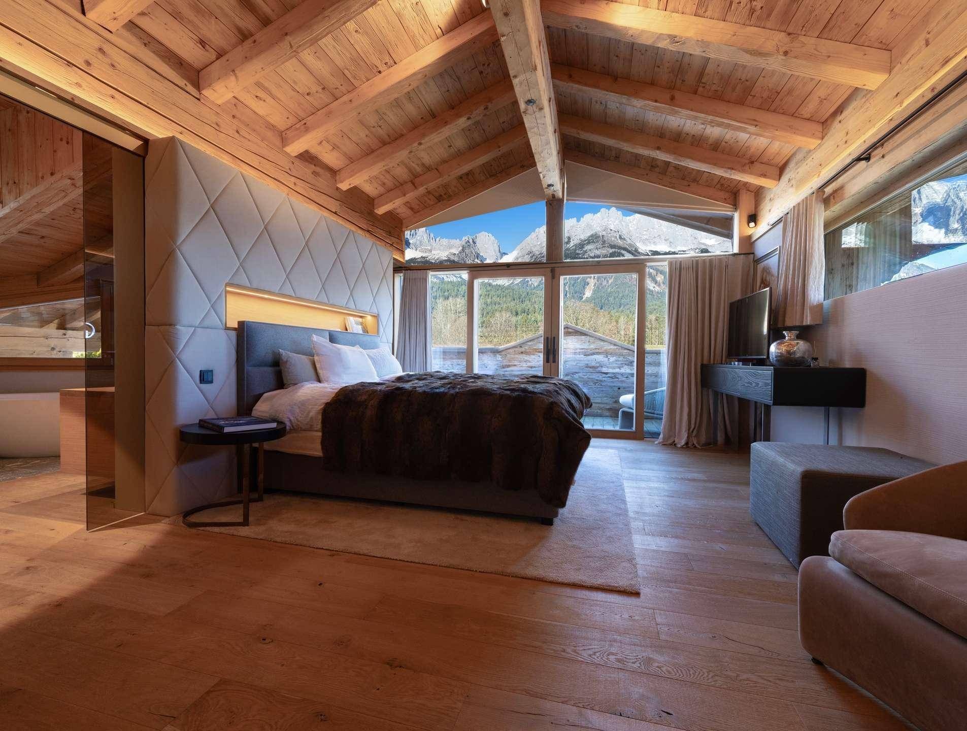 Geräumiges Schlafzimmer mit Holzbalkendecke, großem Bett und Panoramafenstern mit Bergblick.