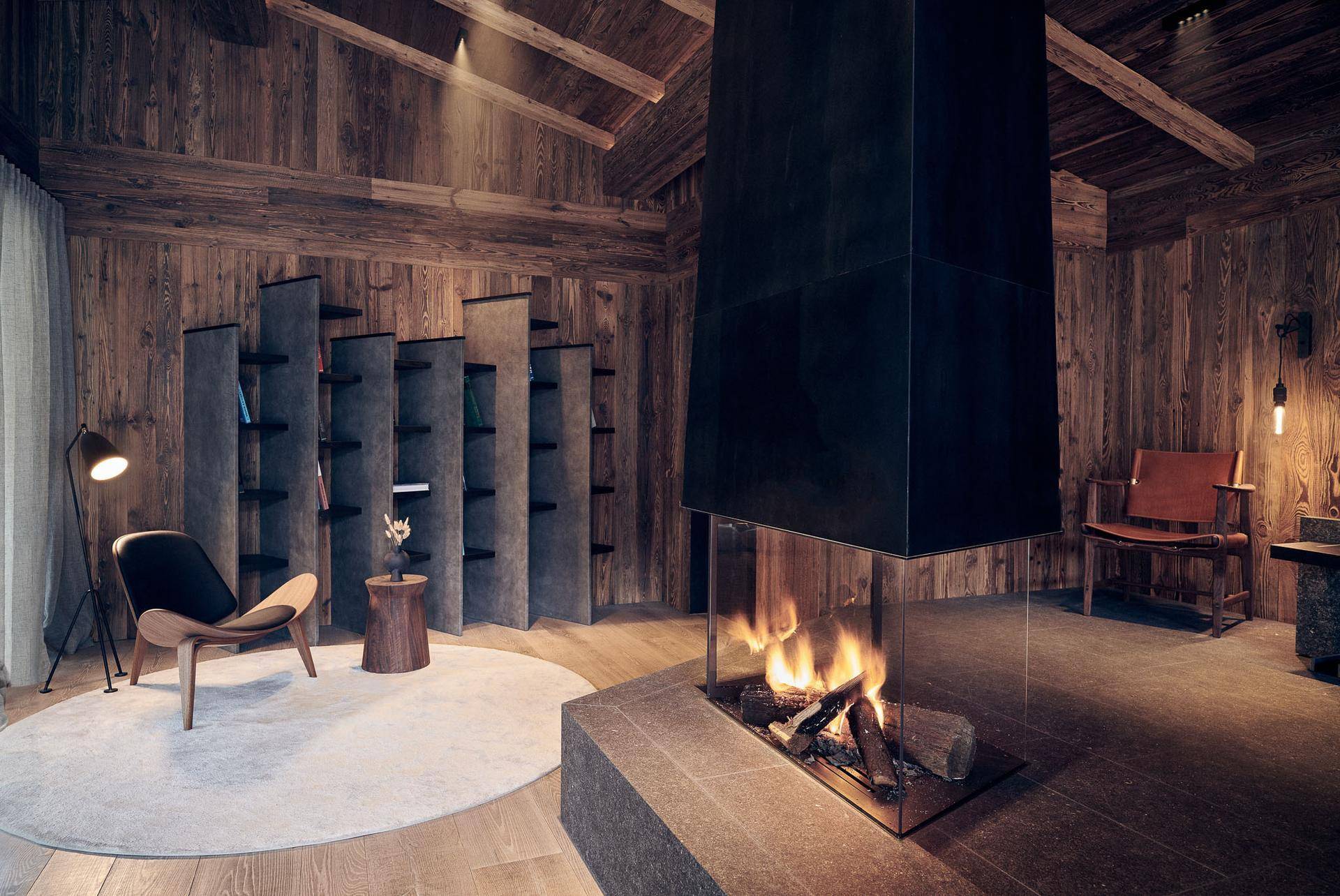 Gemütlicher Wohnbereich mit Holzwänden, Holzbalkendecke und einem modernen, freistehenden Kamin.