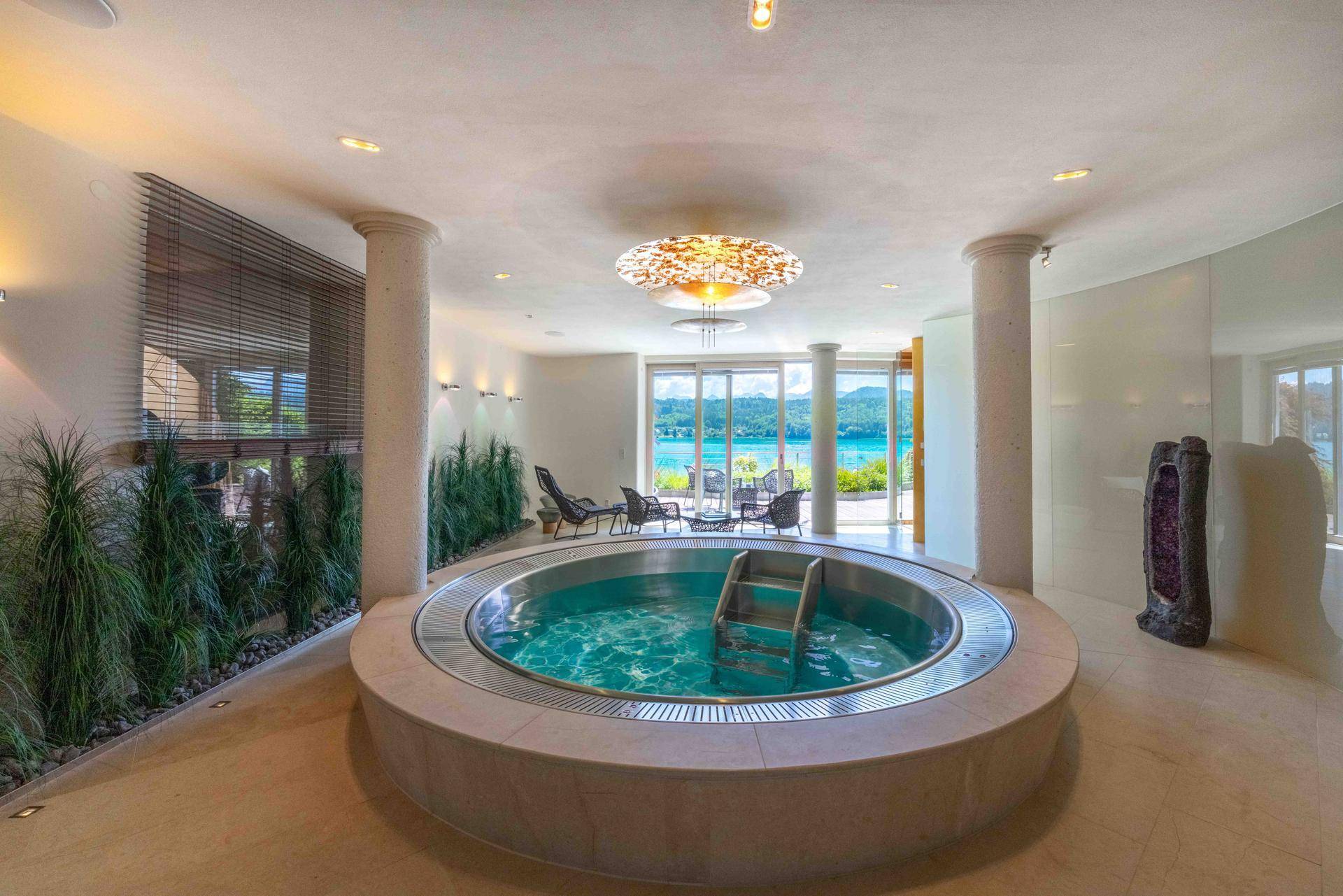 Exklusiver Wellnessbereich mit großem Whirlpool, Säulen und Zugang zu einer Terrasse mit Seeblick.