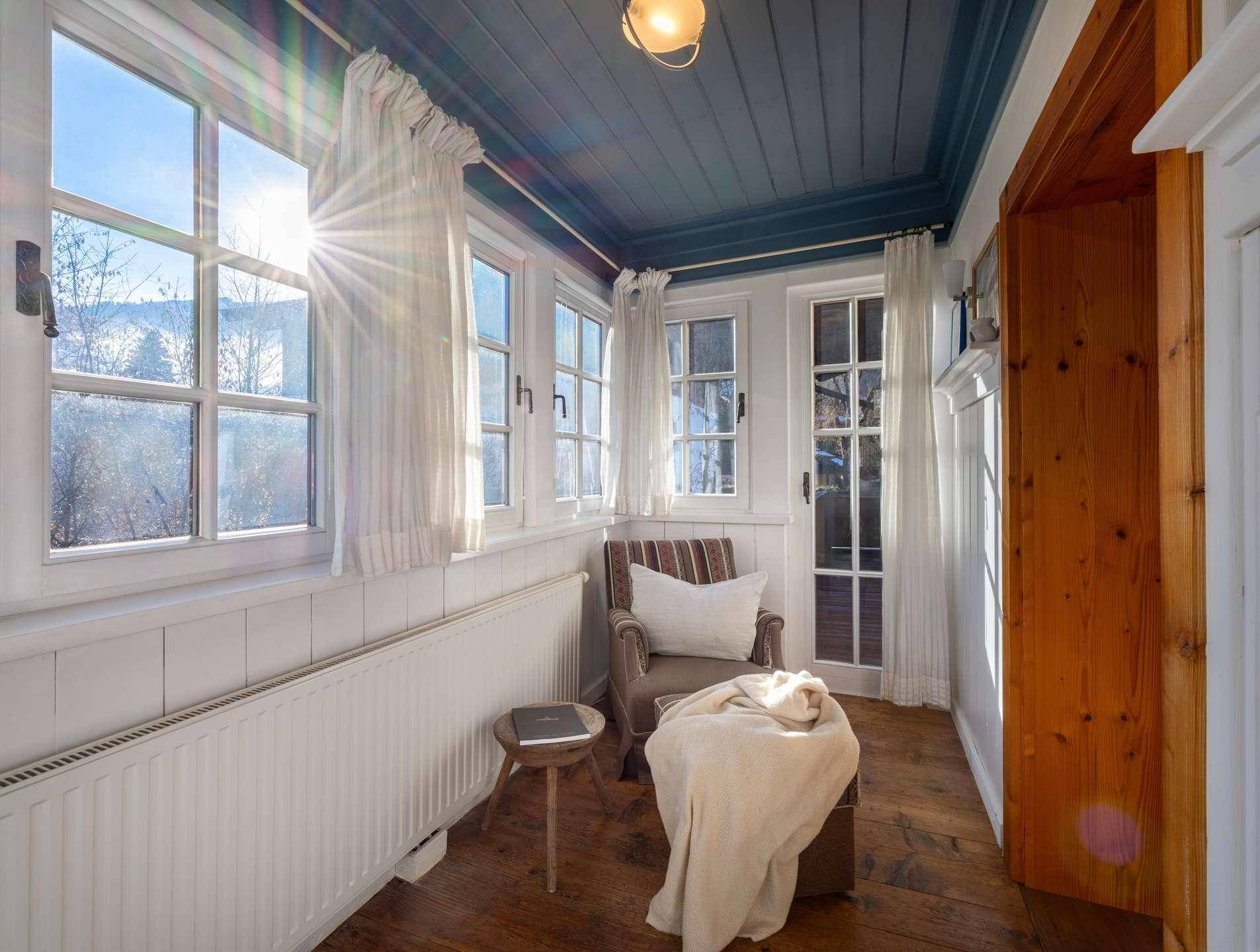 Heller, sonniger Wintergarten mit vielen Fenstern, Holzboden und weitem Ausblick.