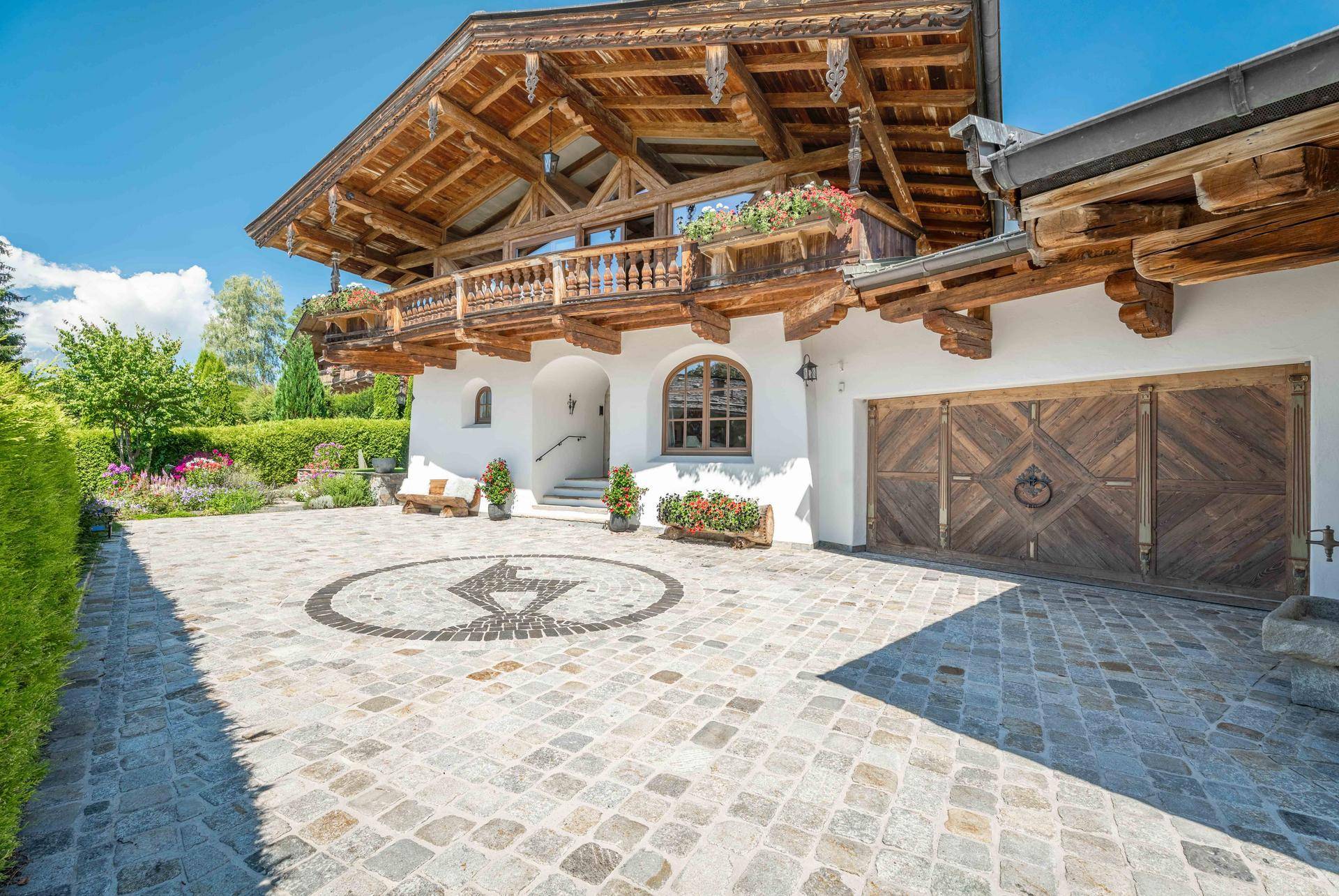 Eingangsbereich eines traditionellen Chalets mit gepflastertem Hof, Holztoren und Balkon.