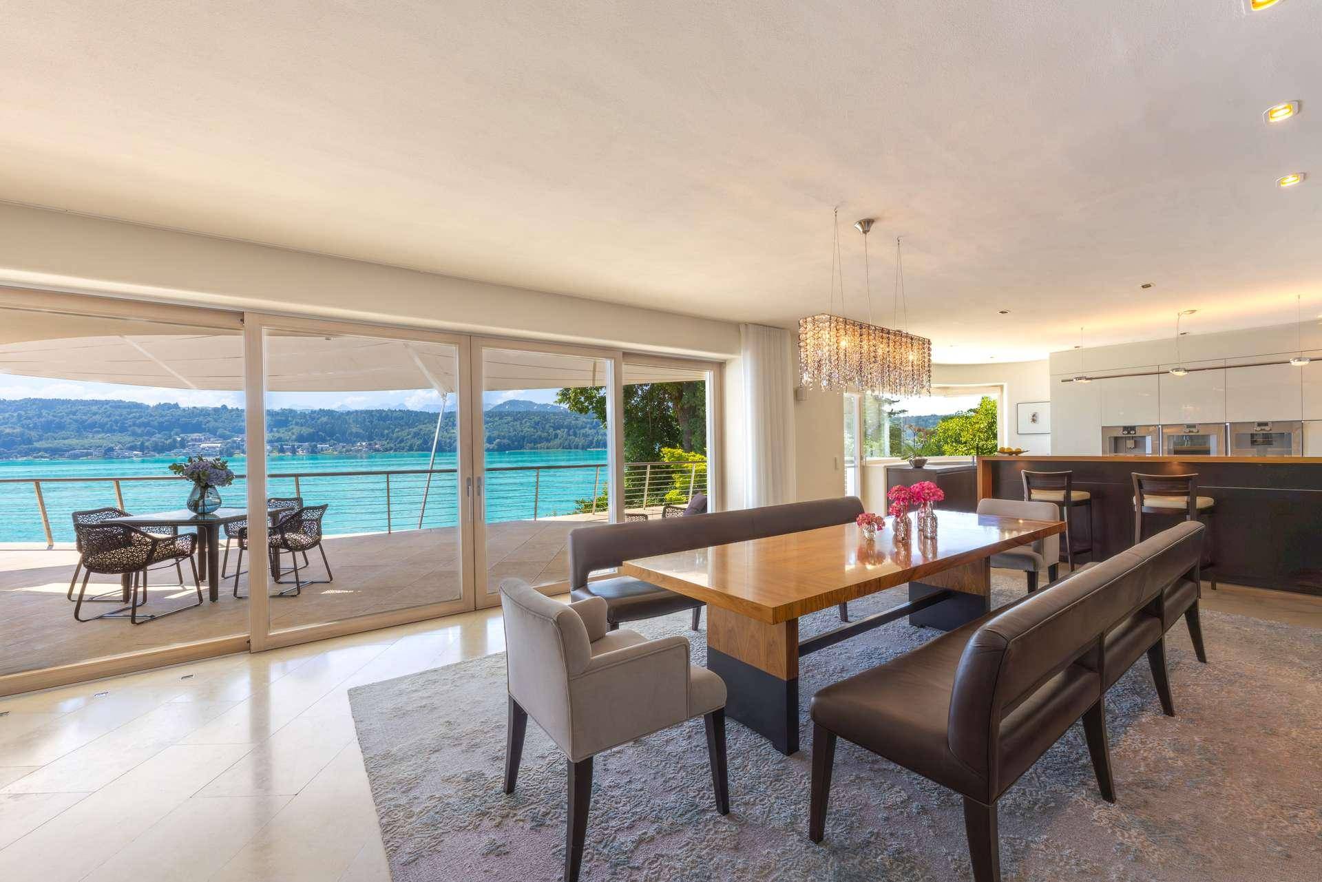Eleganter Essbereich mit Holztisch und Designleuchte, offen zur Küche und mit direktem Zugang zur Terrasse mit Seeblick.