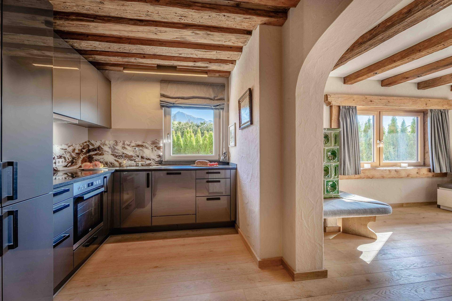 Moderne Küche mit dunklen Fronten, Holzbalkendecke und Fenster mit Bergblick.