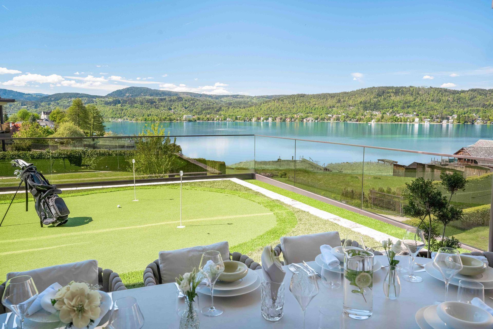 Elegante Terrasse mit Esstisch, weitem Seeblick und privatem Putting Green im Gartenbereich.