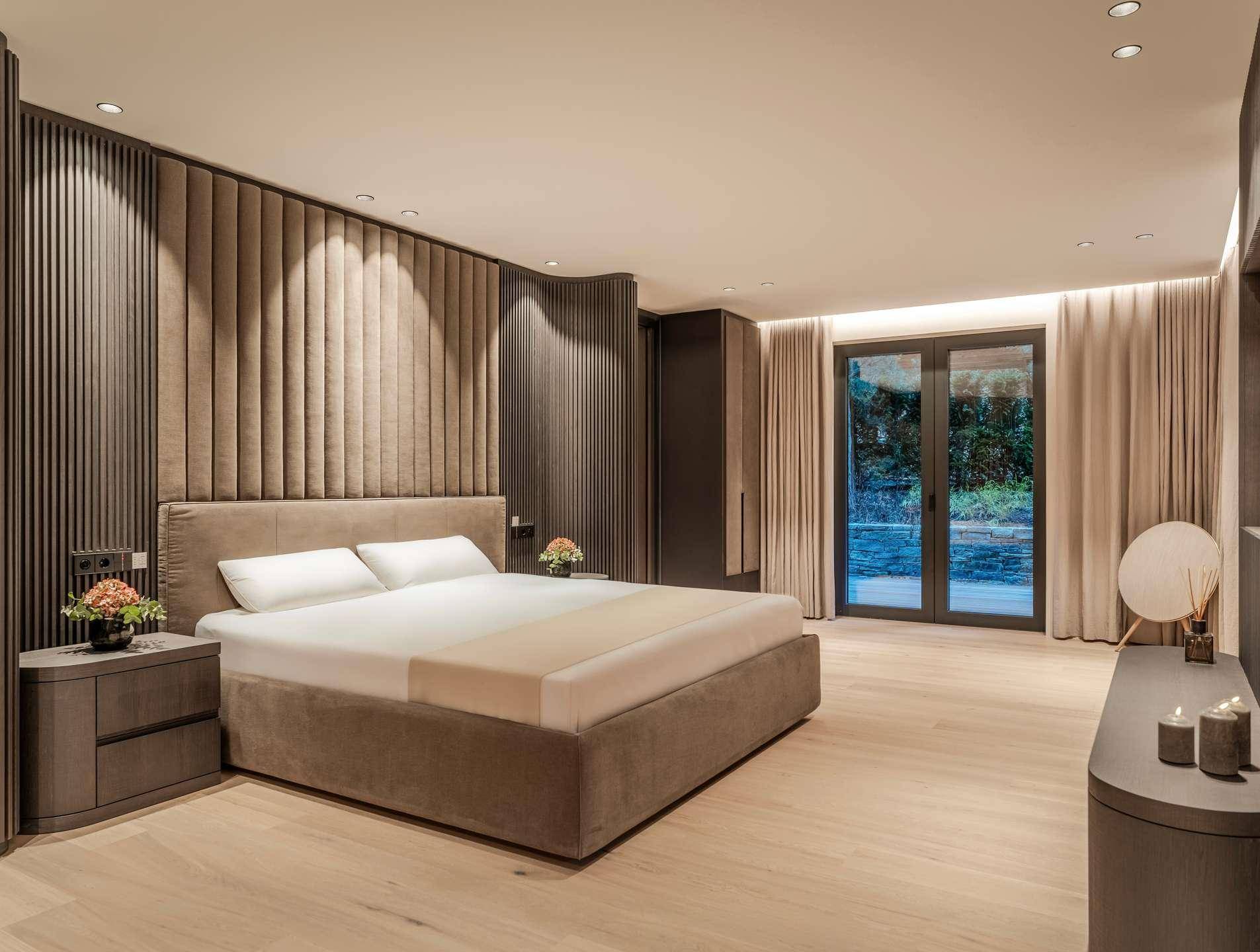 Elegantes Schlafzimmer mit gepolsterter Wand, Holzboden und Zugang zu einem Außenbereich.