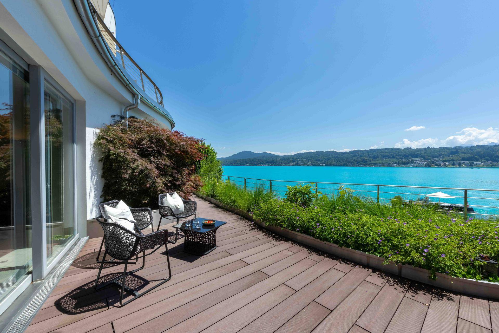Holzterrasse mit modernen Sitzgelegenheiten, Pflanzen und weitem Blick über den See.