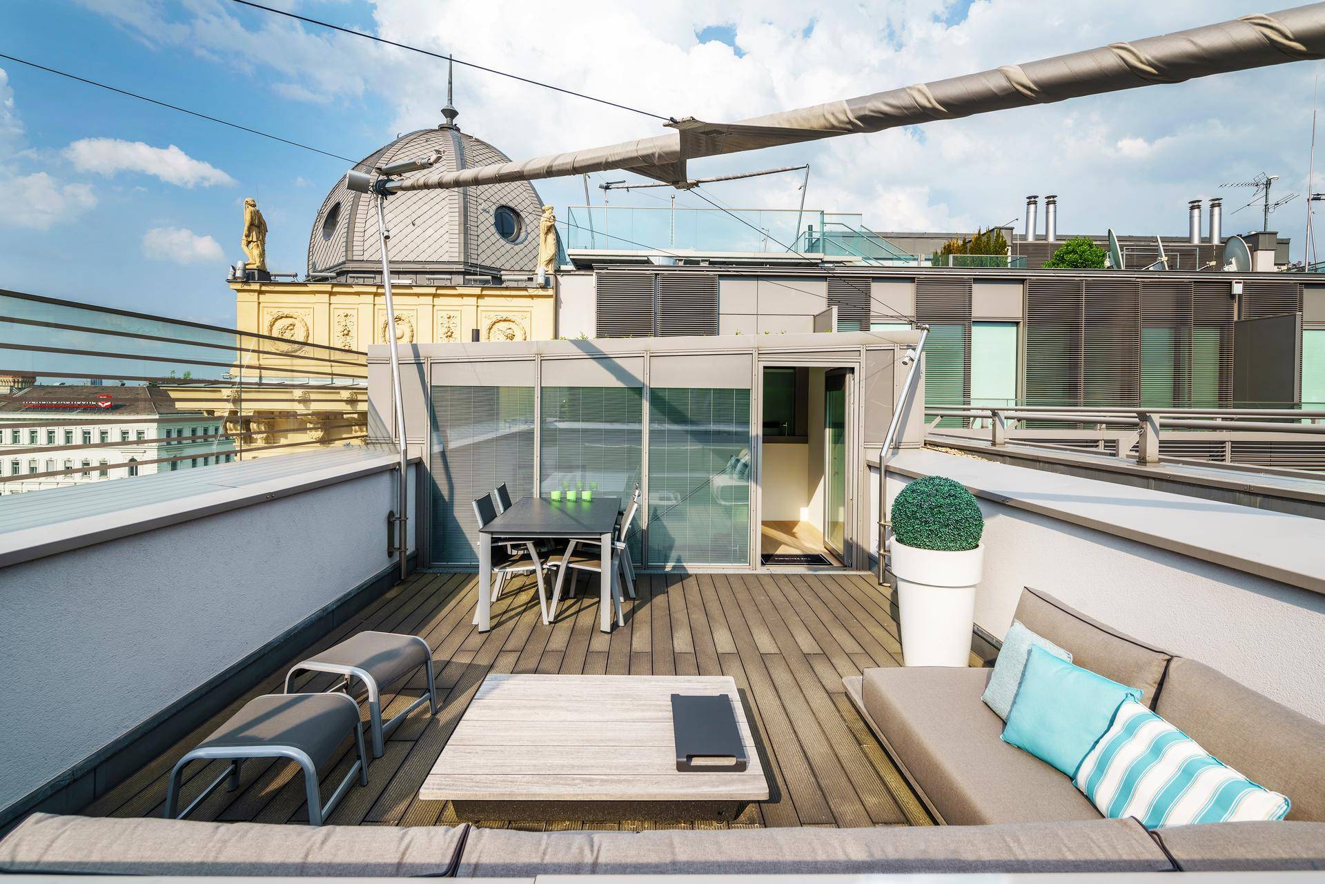 Geräumige Dachterrasse mit Holzboden, bequemen Loungemöbeln und Blick auf historische Stadtgebäude.
