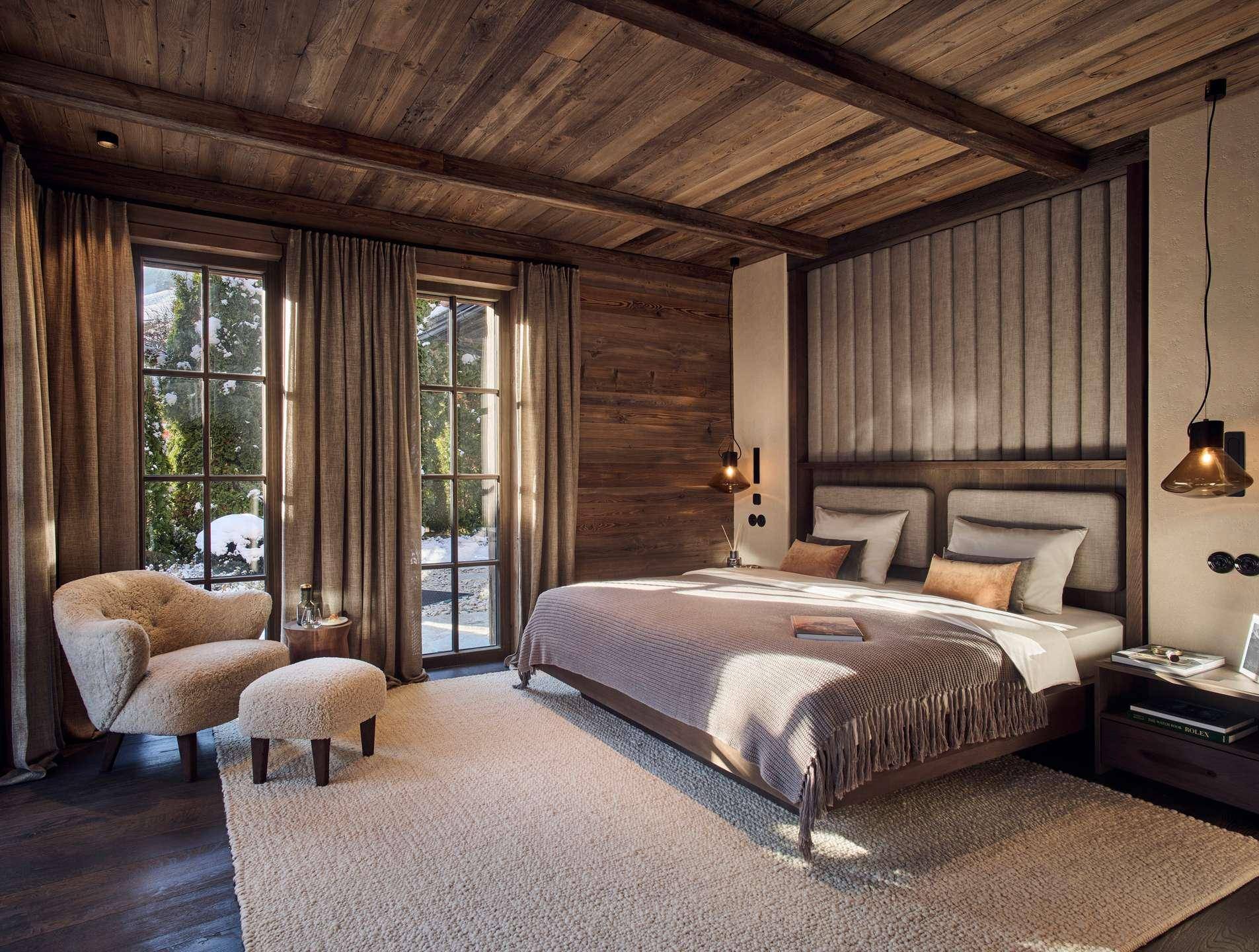 Luxuriöses Schlafzimmer im alpinen Stil mit Holzwänden, großen Fenstern und Blick ins Grüne.