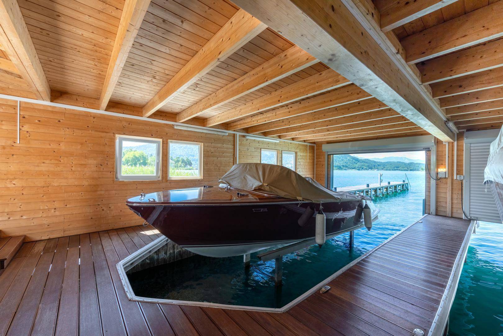 Rustikales Bootshaus mit Holzbalken, Bootslift und direktem Zugang zum See.