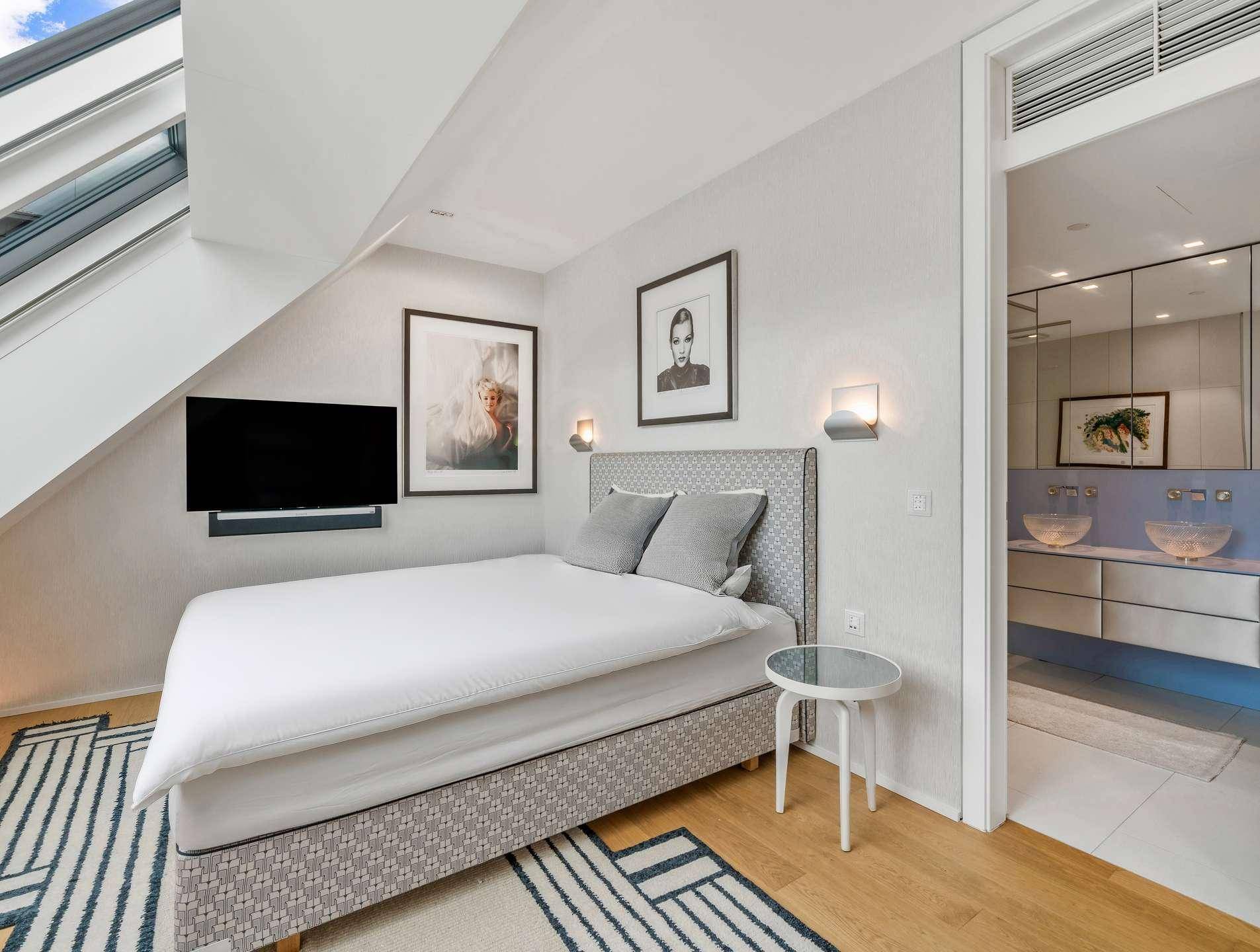 Schlafzimmer im Dachgeschoss mit Holzboden, Fernseher und direktem Zugang zum Badezimmer.