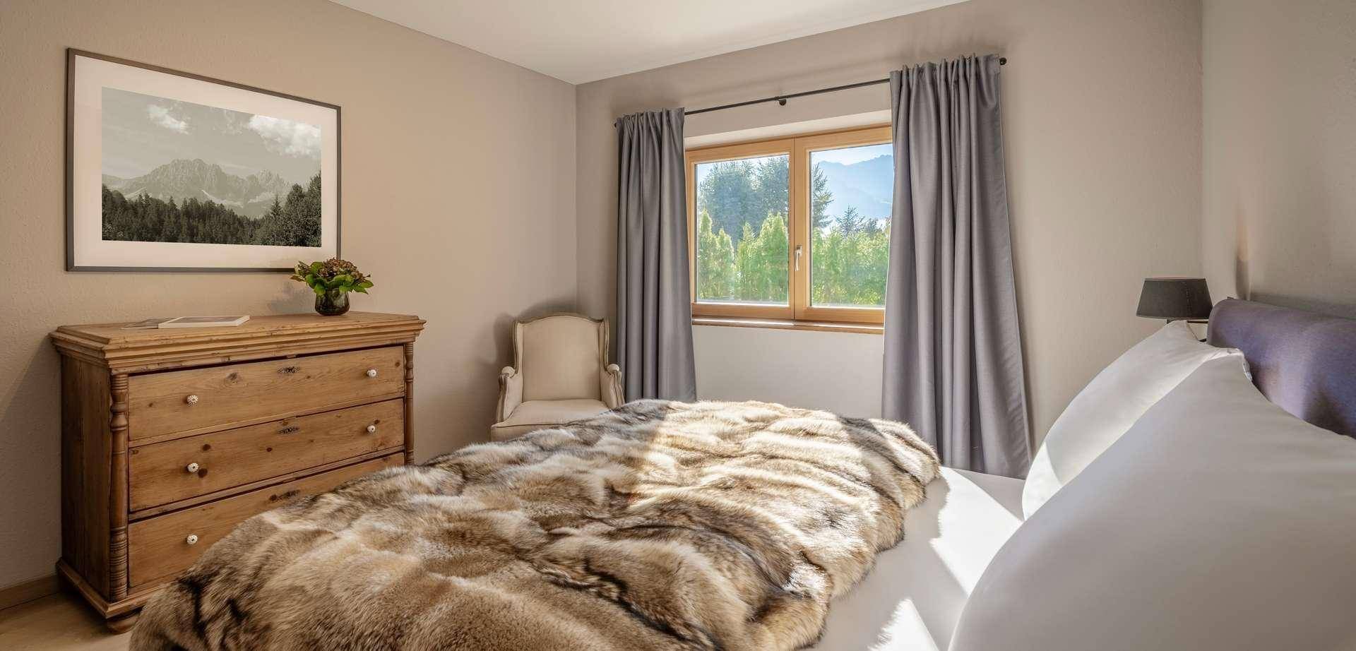 Gemütliches Schlafzimmer mit Holzkleiderschrank, weicher Decke und Bergblick.
