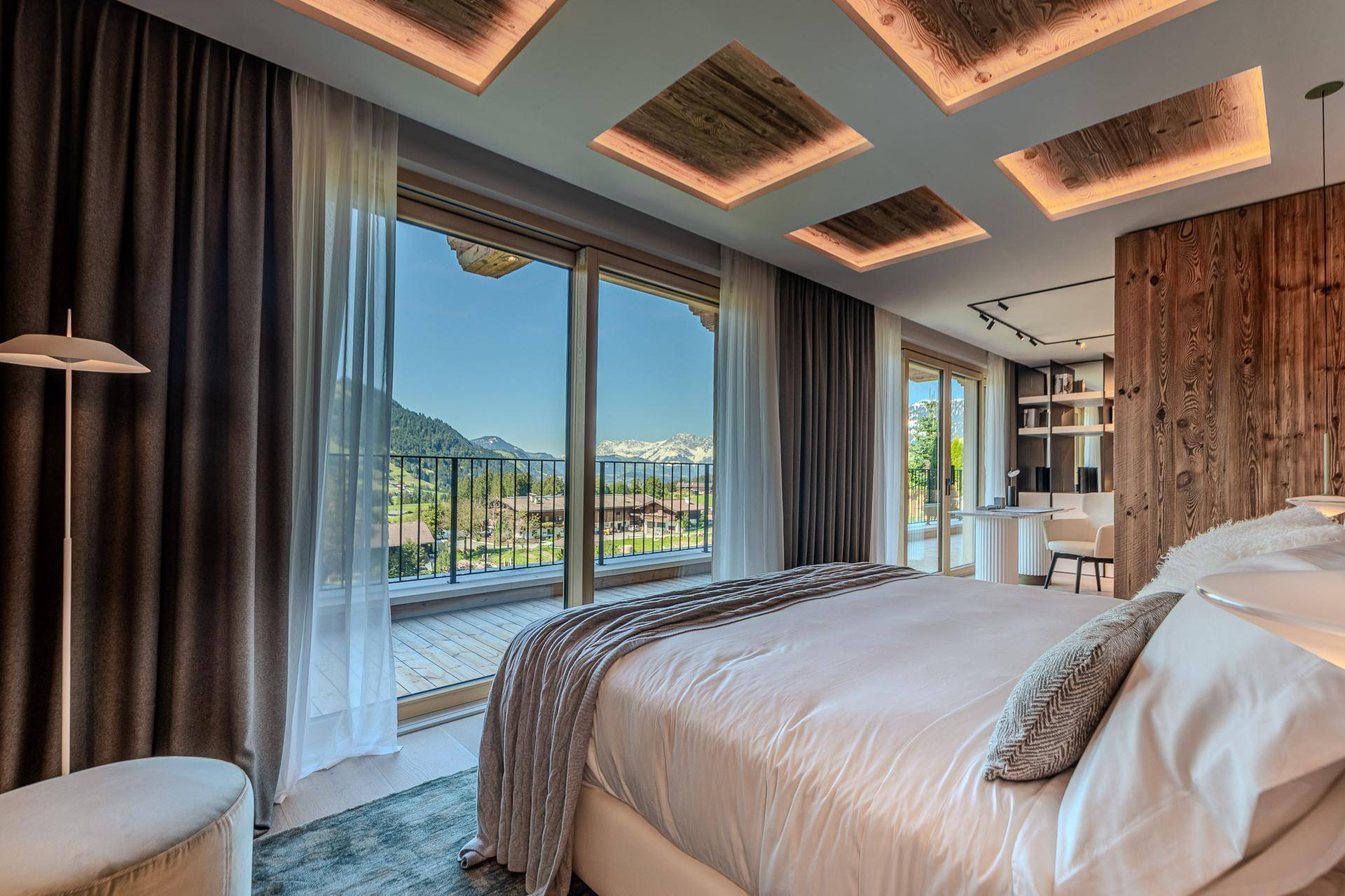 Helles Schlafzimmer mit Balkonzugang, Holzwand und atemberaubendem Bergblick.