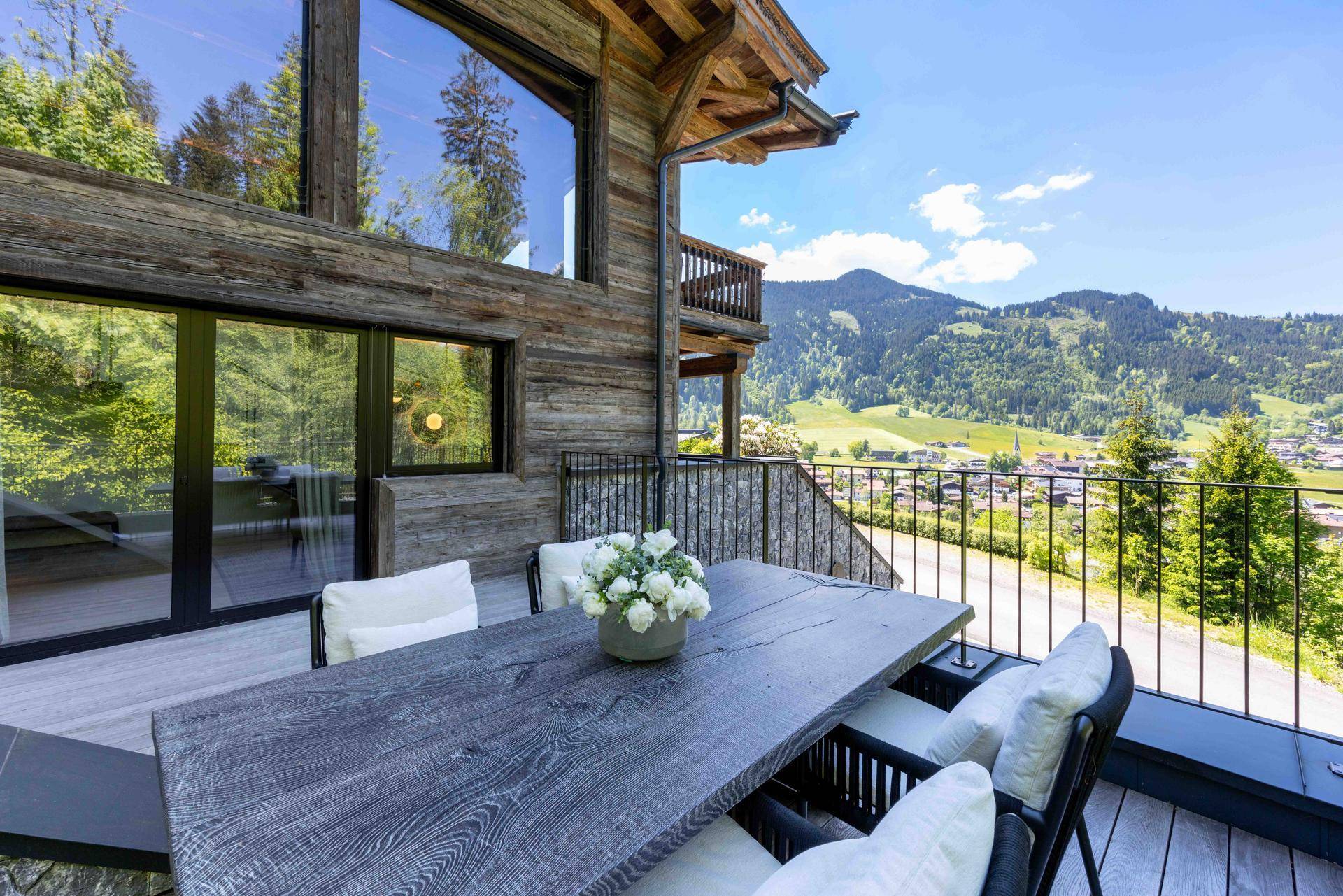 Sonniger Außenbereich mit Esstisch und Stühlen, umgeben von alpiner Landschaft und Bergblick.