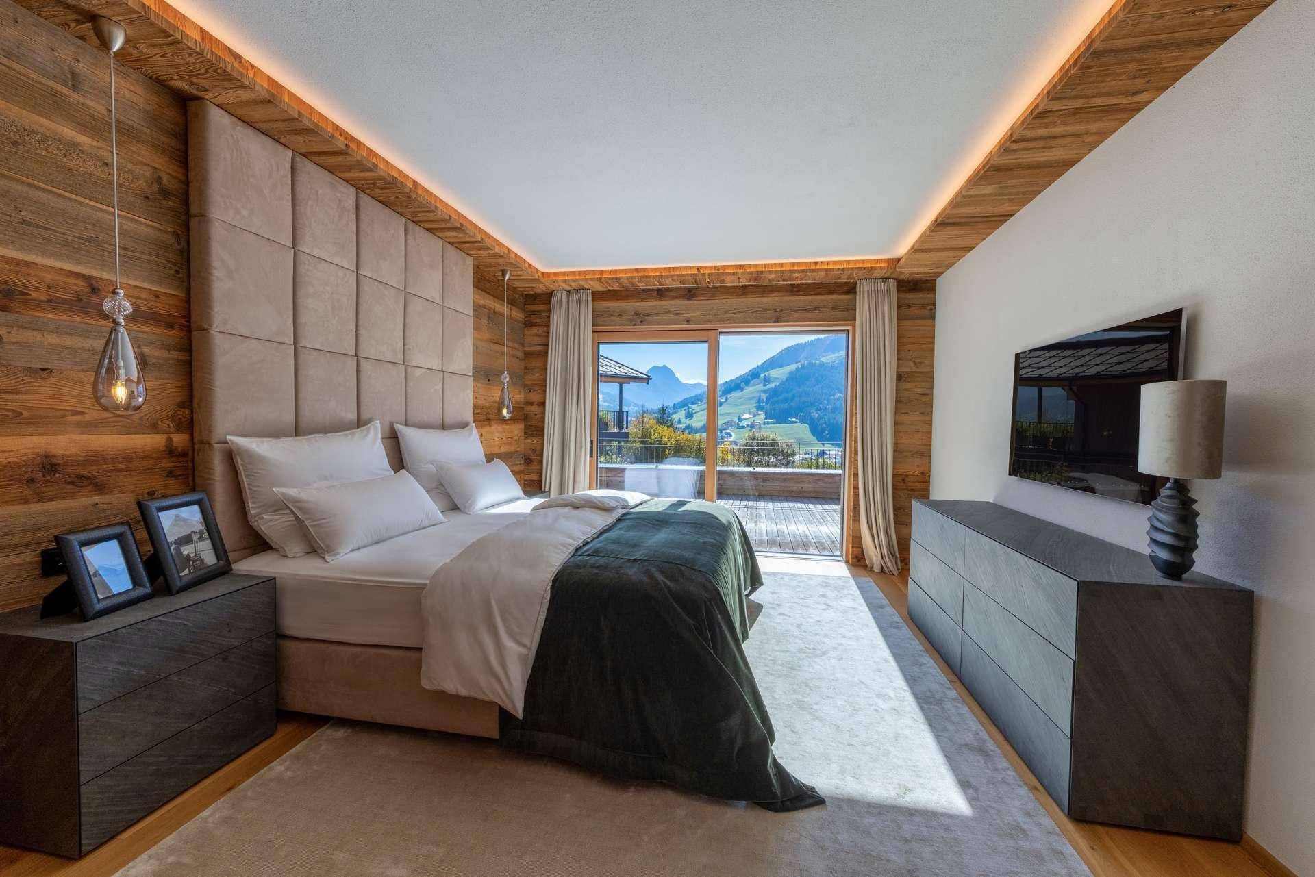 Modernes Schlafzimmer mit Holzwänden, gepolstertem Kopfteil und Zugang zu einem Balkon mit Bergblick.