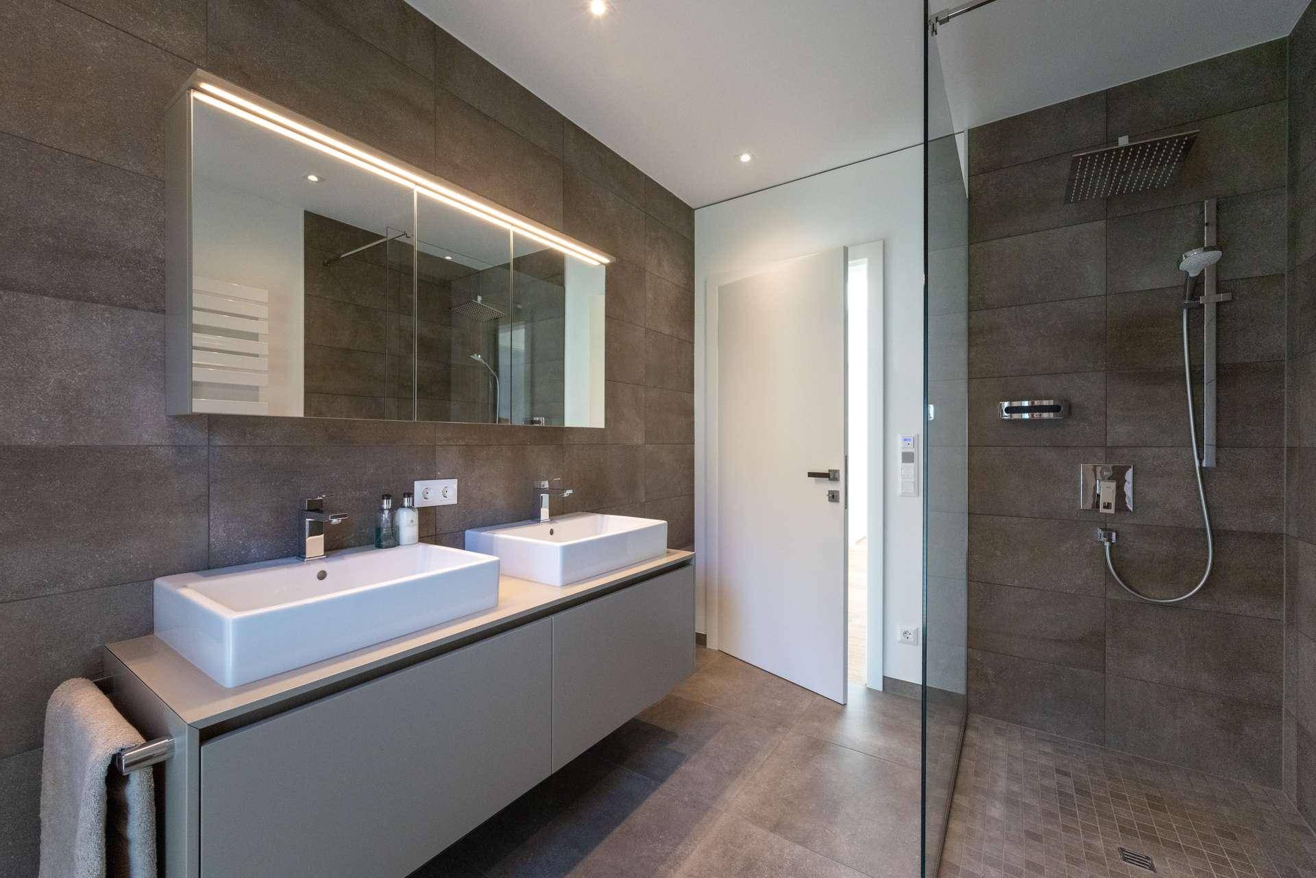 Modernes Badezimmer mit Doppelwaschbecken, großer begehbarer Dusche und dunklen Fliesen.