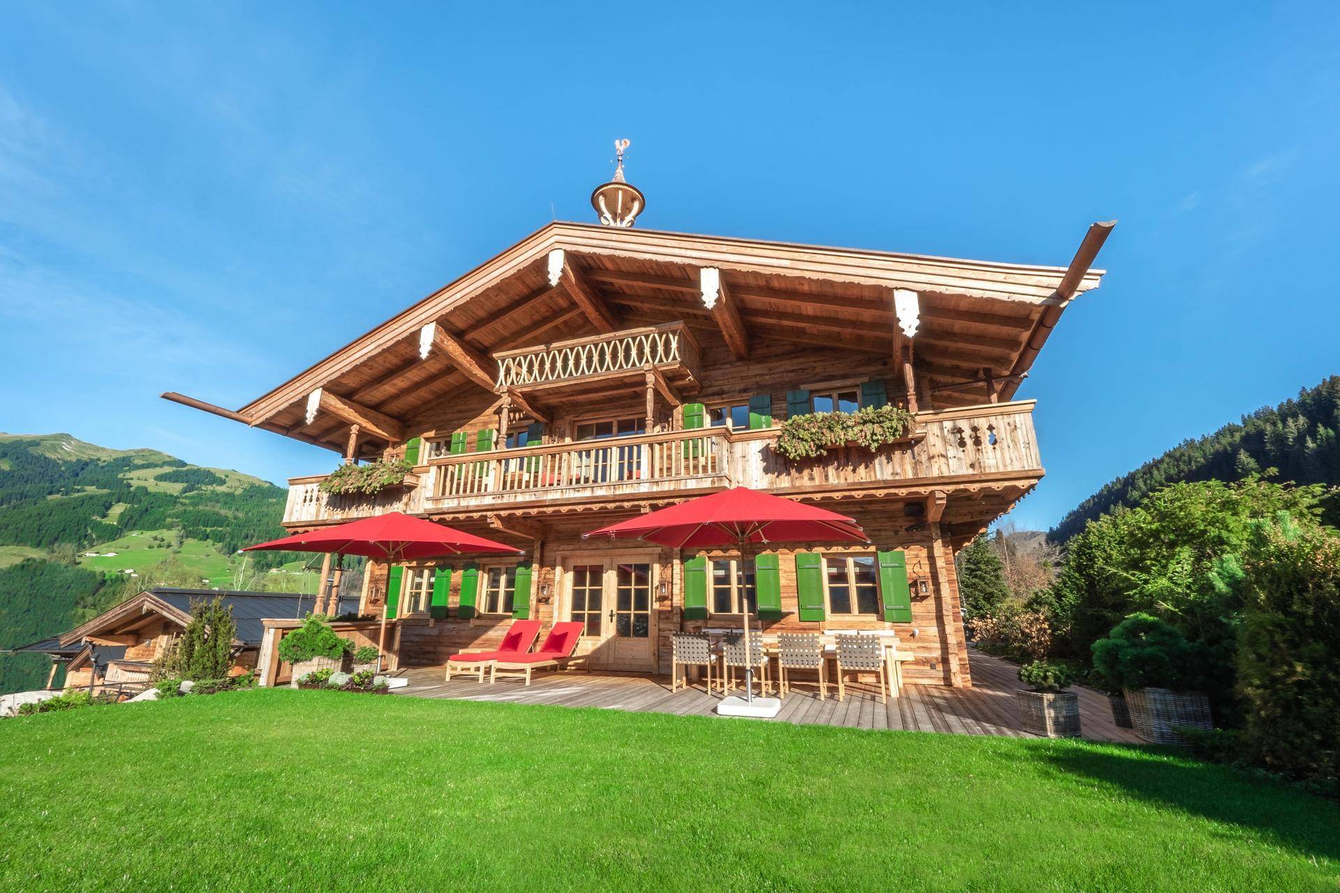 Charmantes Alpenchalet mit großer Rasenfläche und möbliertem Außenbereich unter blauem Himmel.