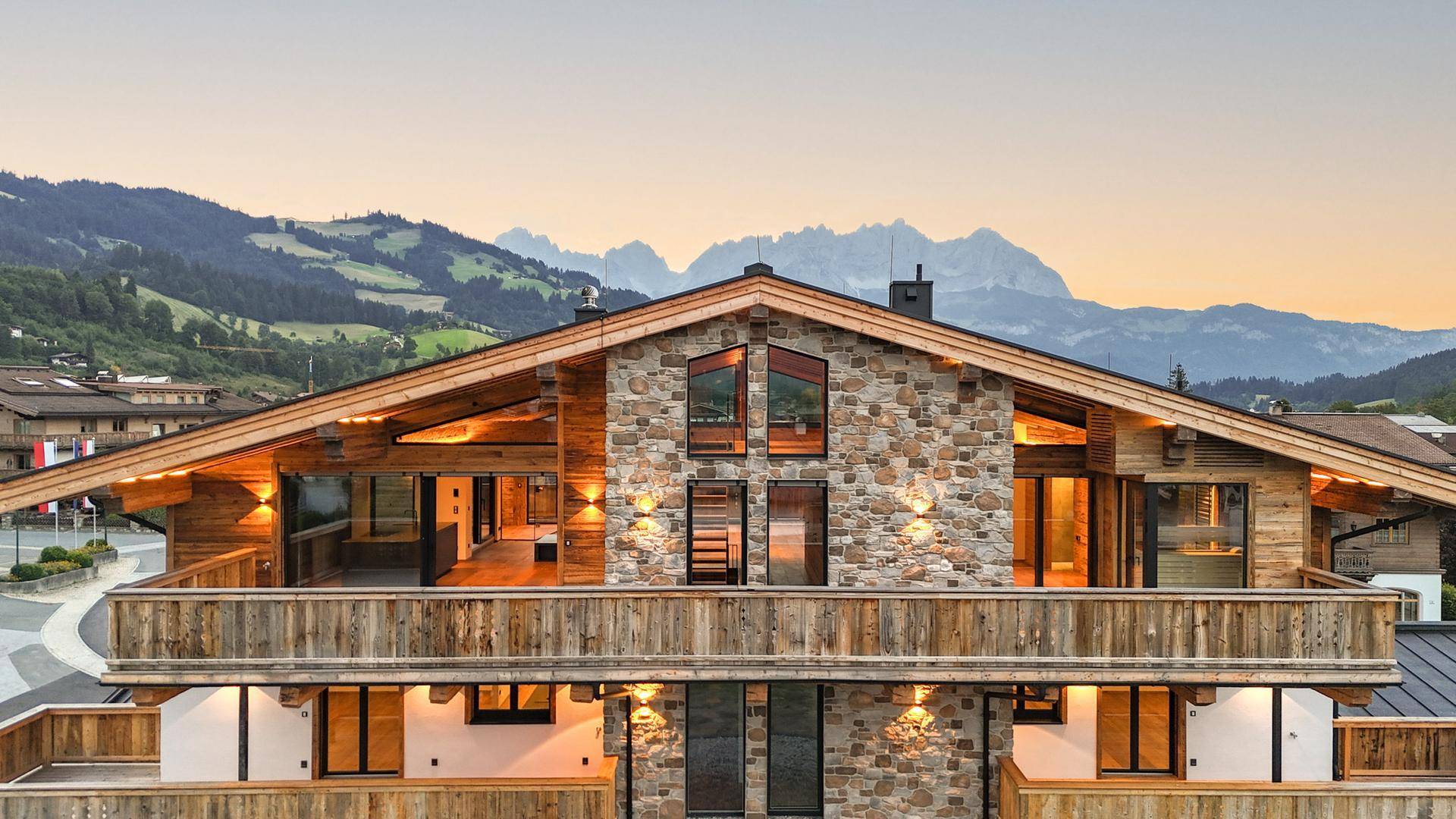 Beeindruckende Chalet-Fassade mit Stein- und Holzelementen sowie breiten Balkonen und Bergblick.