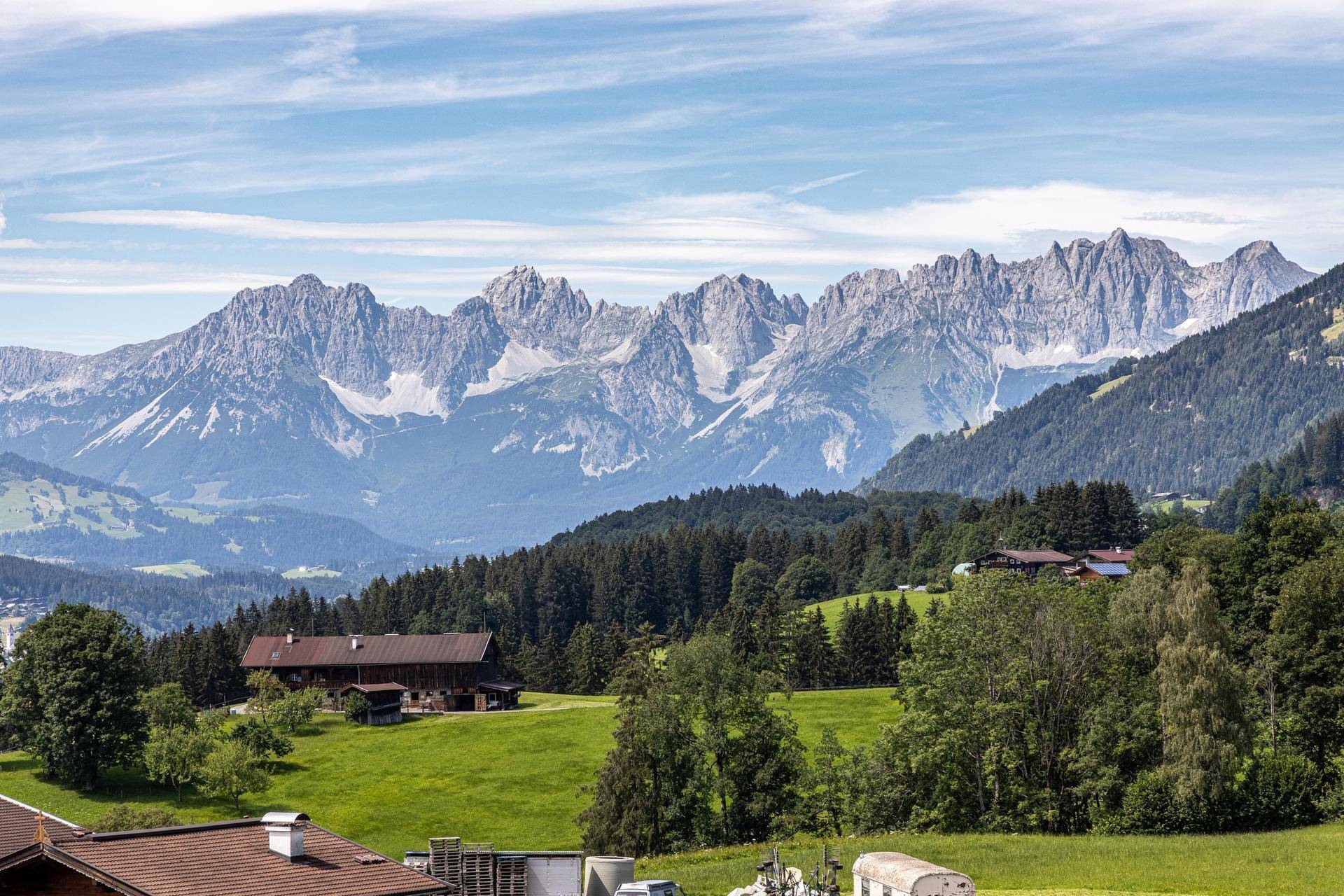 Weitläufige Berglandschaft mit grünen Wiesen und Wäldern unter blauem Himmel.