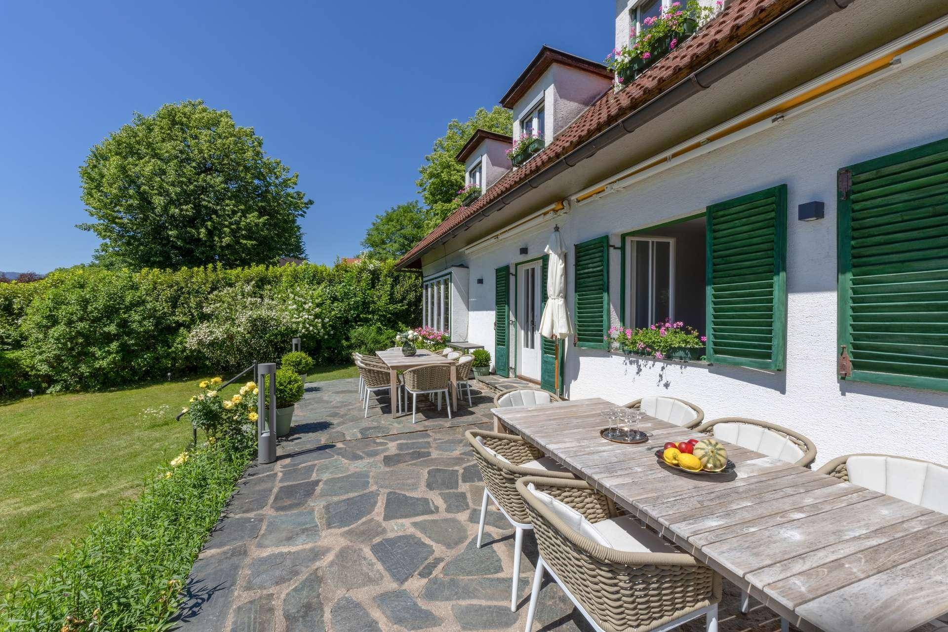 Rustikale Steinterrasse mit mehreren Essbereichen und Blick auf den gepflegten Garten und die grüne Umgebung.