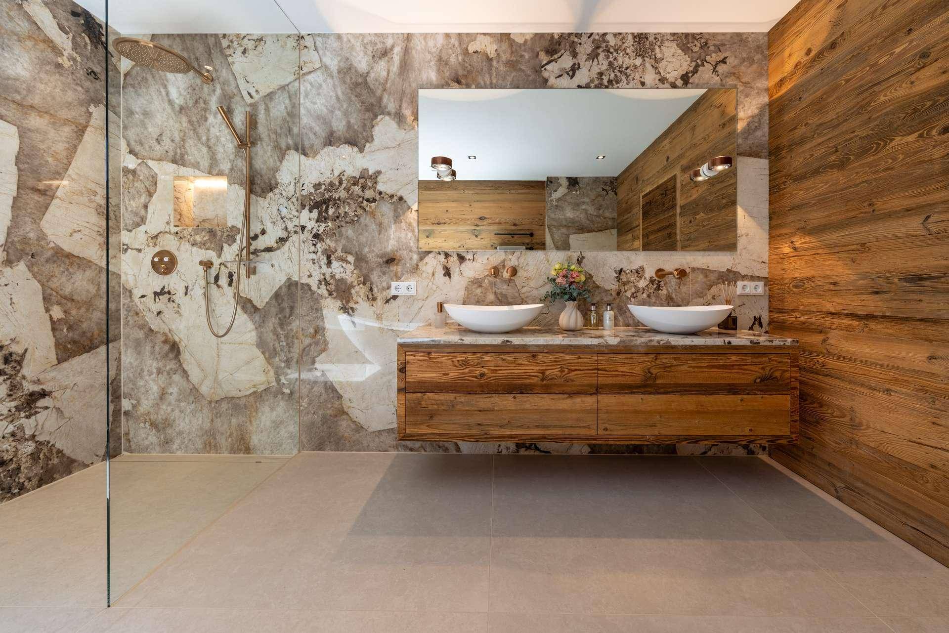 Elegantes Badezimmer mit doppelten Waschbecken, begehbarer Dusche und Natursteinwänden im modernen Design.