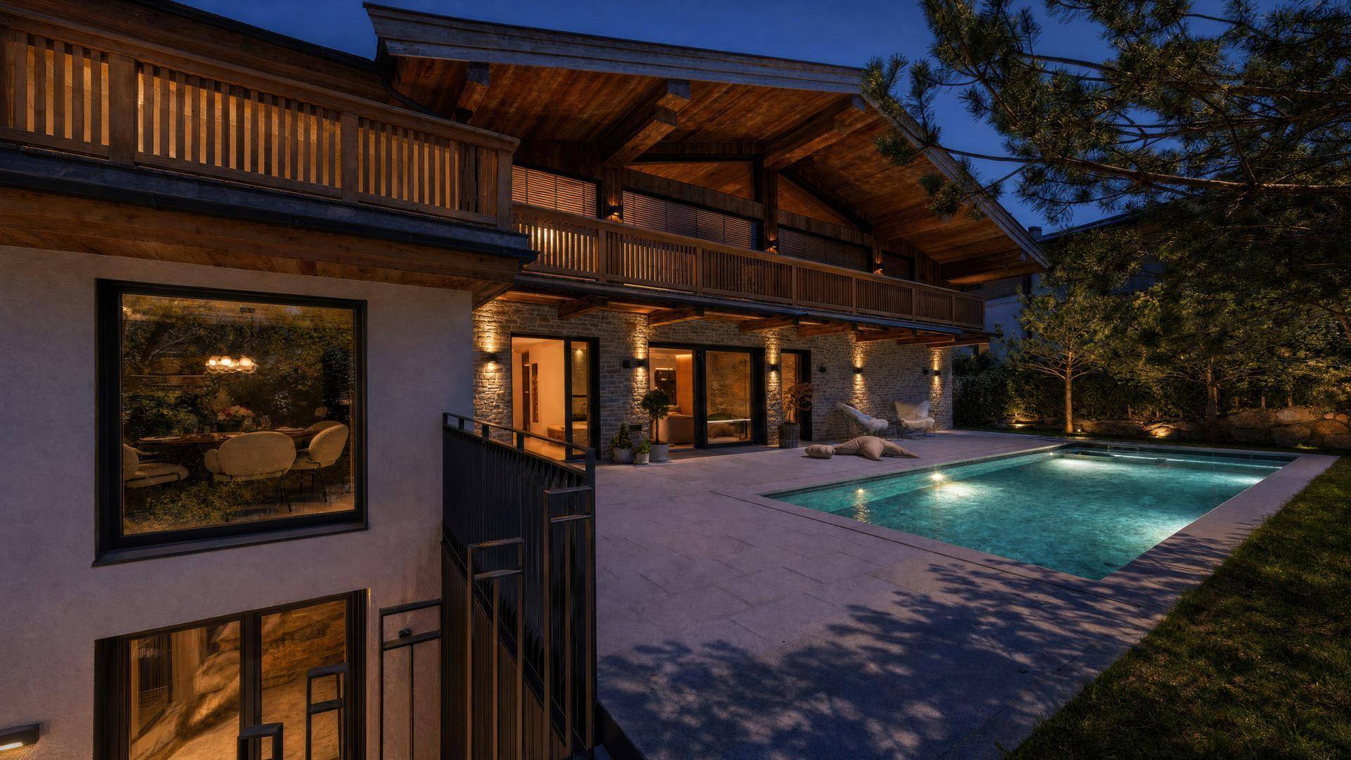 Beleuchtetes Chalet mit Pool und Terrasse bei Nacht, umgeben von stimmungsvoller Außenbeleuchtung.