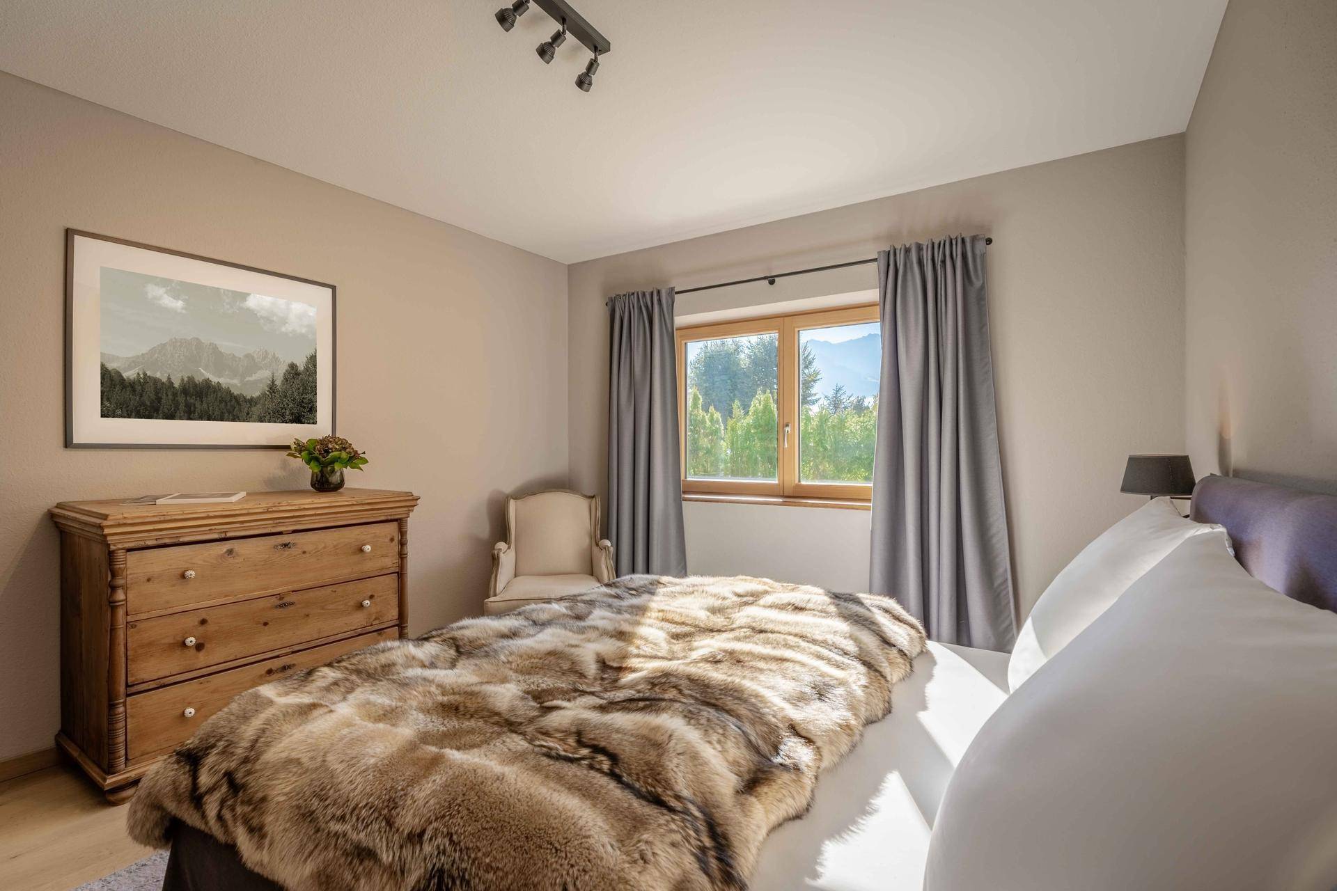 Gemütliches Schlafzimmer mit Holzkleiderschrank, großem Bett und Fenster mit Bergblick.