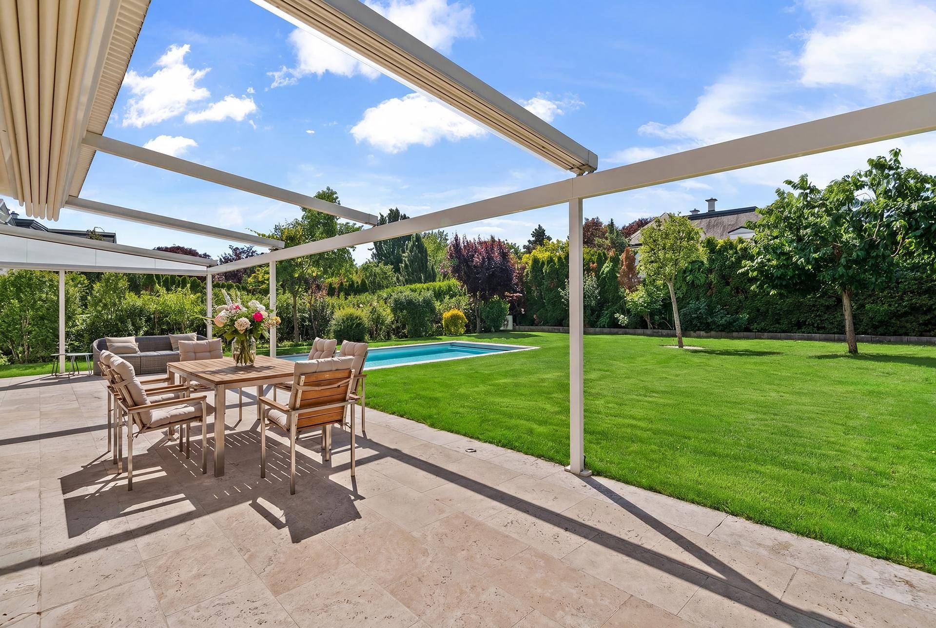 Große, überdachte Terrasse mit Essbereich, Blick auf den Pool und den gepflegten Garten.