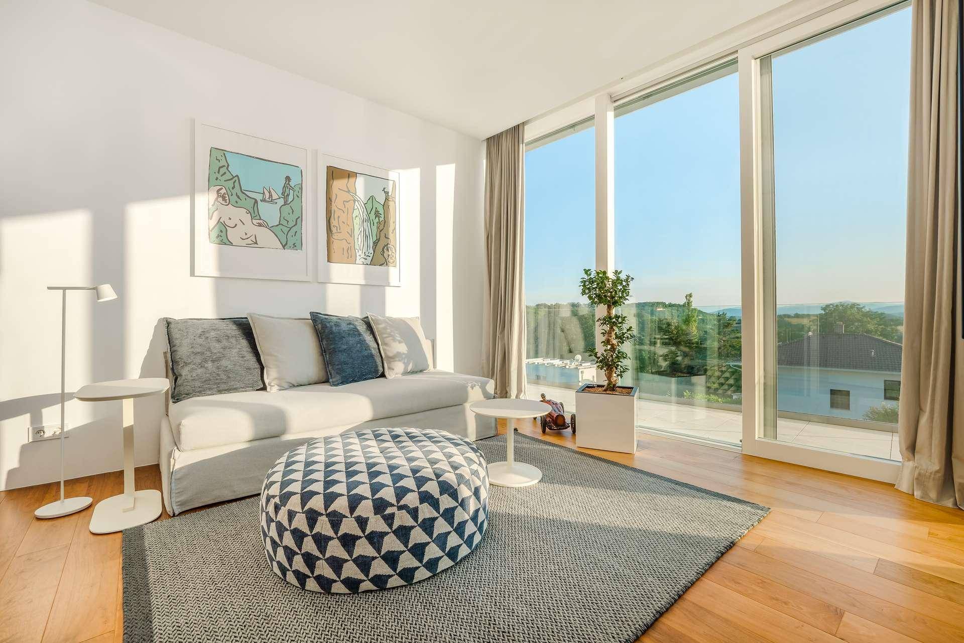 Gemütliches Wohnzimmer mit Sofa, modernem Pouf und raumhohen Fenstern mit Panoramablick.