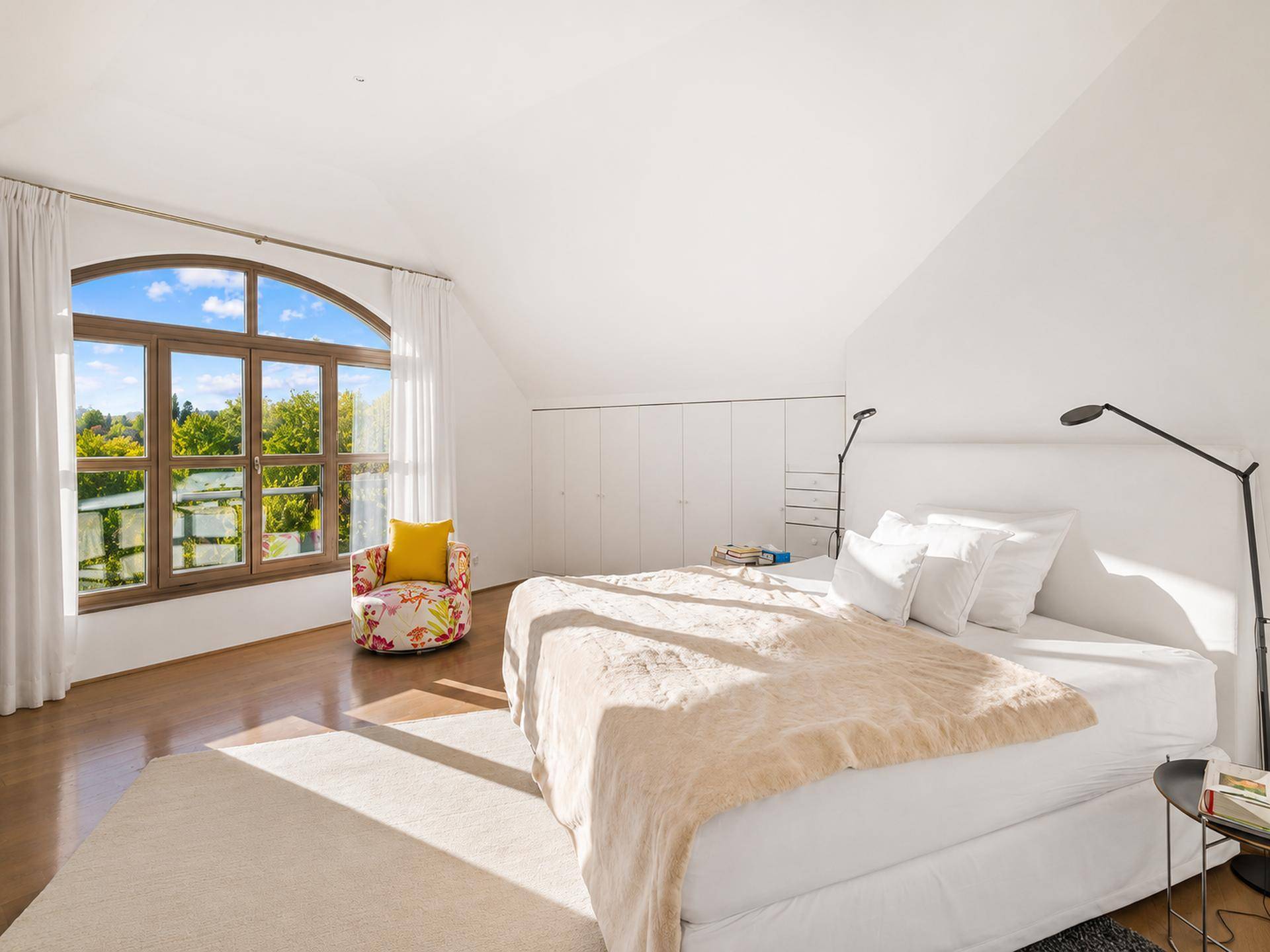 Geräumiges, helles Schlafzimmer mit großem Rundbogenfenster, Holzboden und Einbauschränken.