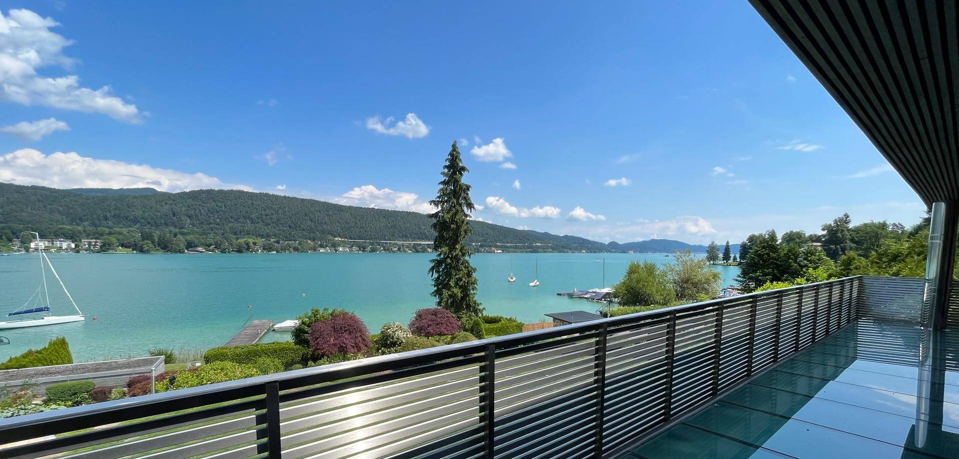 Weitläufiger Balkon mit moderner Glasbrüstung und atemberaubendem Blick über den See und die Landschaft.