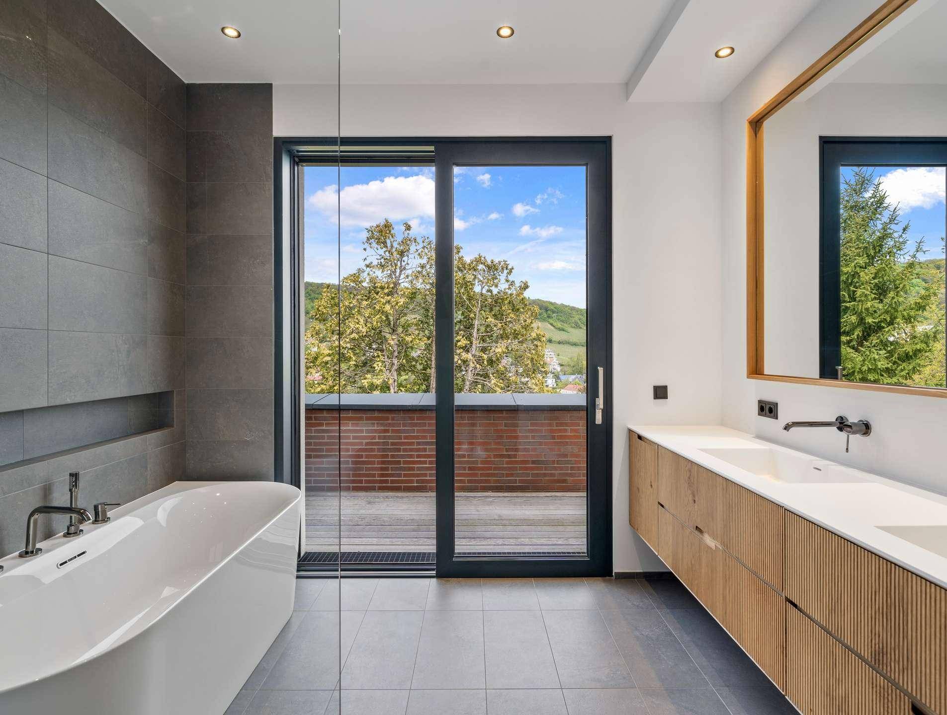 Modernes Badezimmer mit freistehender Badewanne, Doppelwaschbecken und Zugang zur Außenterrasse.