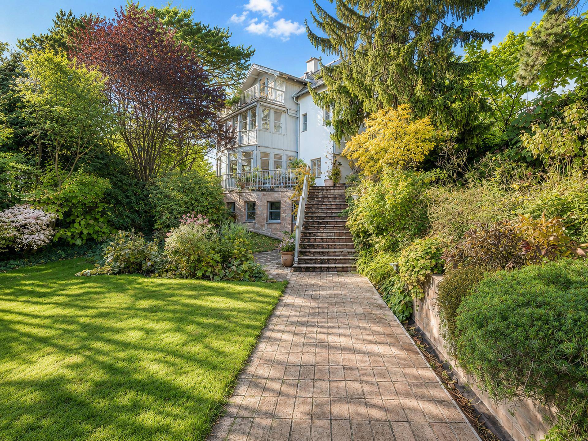 Elegantes Haus mit weitläufigem Garten, Steintreppe und gepflegtem Rasen in sonniger Umgebung.