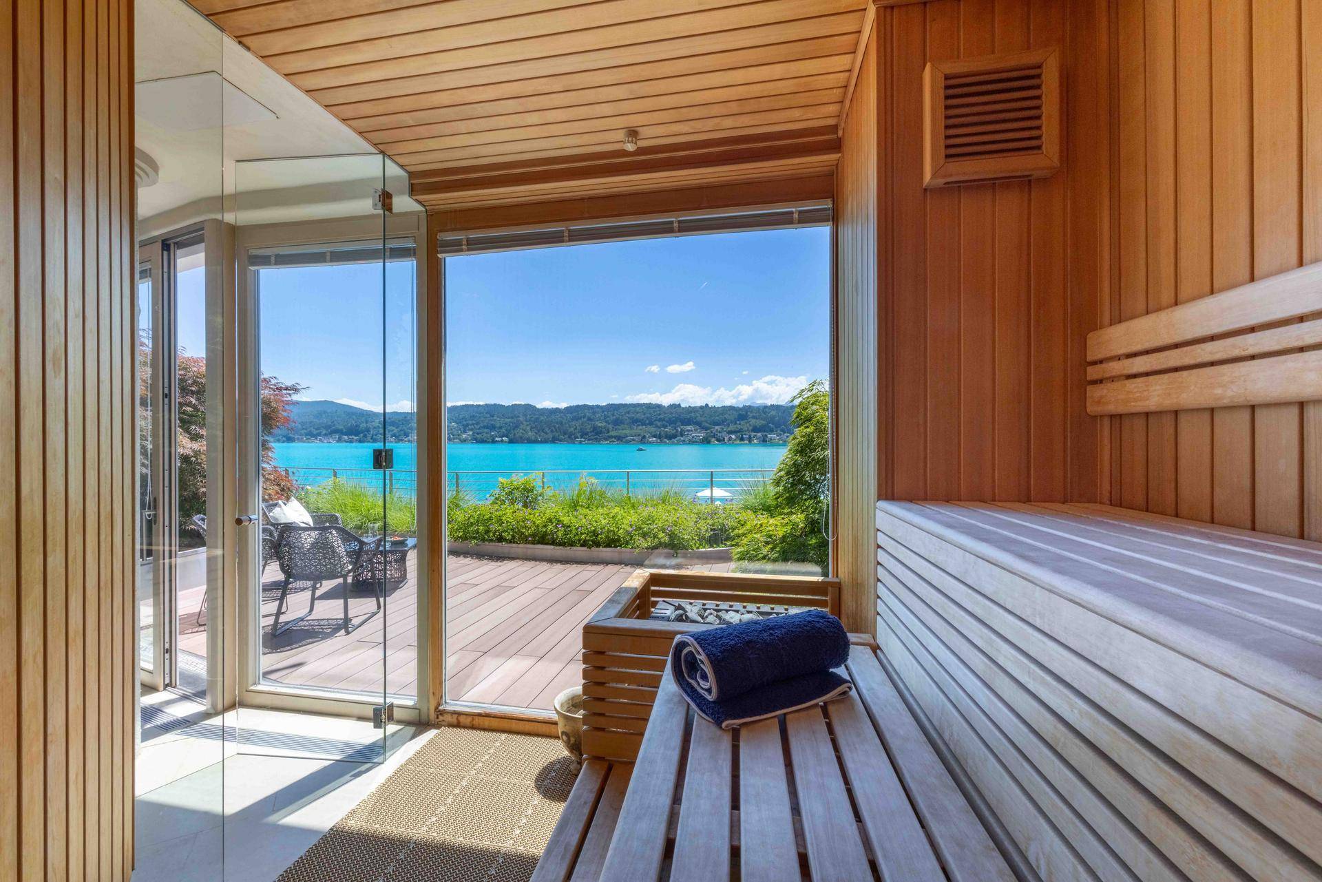 Moderne Sauna mit Holzverkleidung, Sitzbänken und direktem Blick auf den See und die Terrasse.